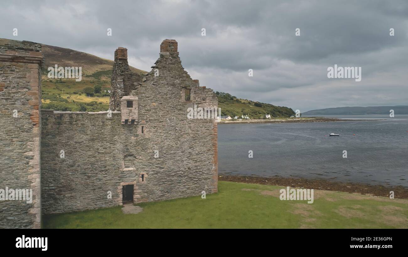 Closeup of ancient castle ruins at sea bay aerial. Nobody nature seascape with boats. Historic heritage. Hamilton dynasty palace on ocean coast of Arran Island, Scotland, UK, Europe. Drone shot Stock Photo