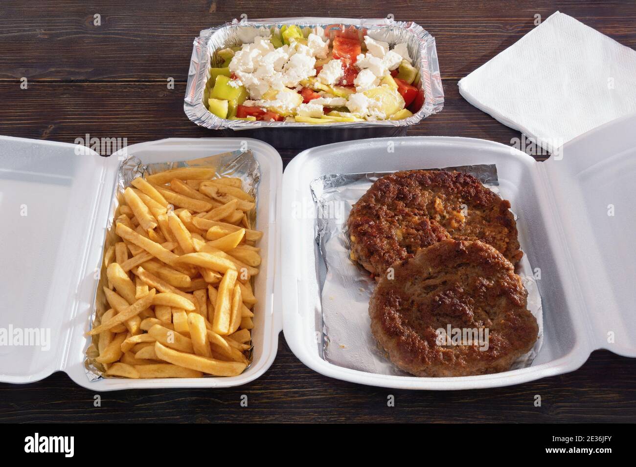 Food delivery. Balkan cuisine. Pljeskavica - grilled dish of minced meat;  french fries and salad in takeaway containers on rustic wooden table Stock Photo