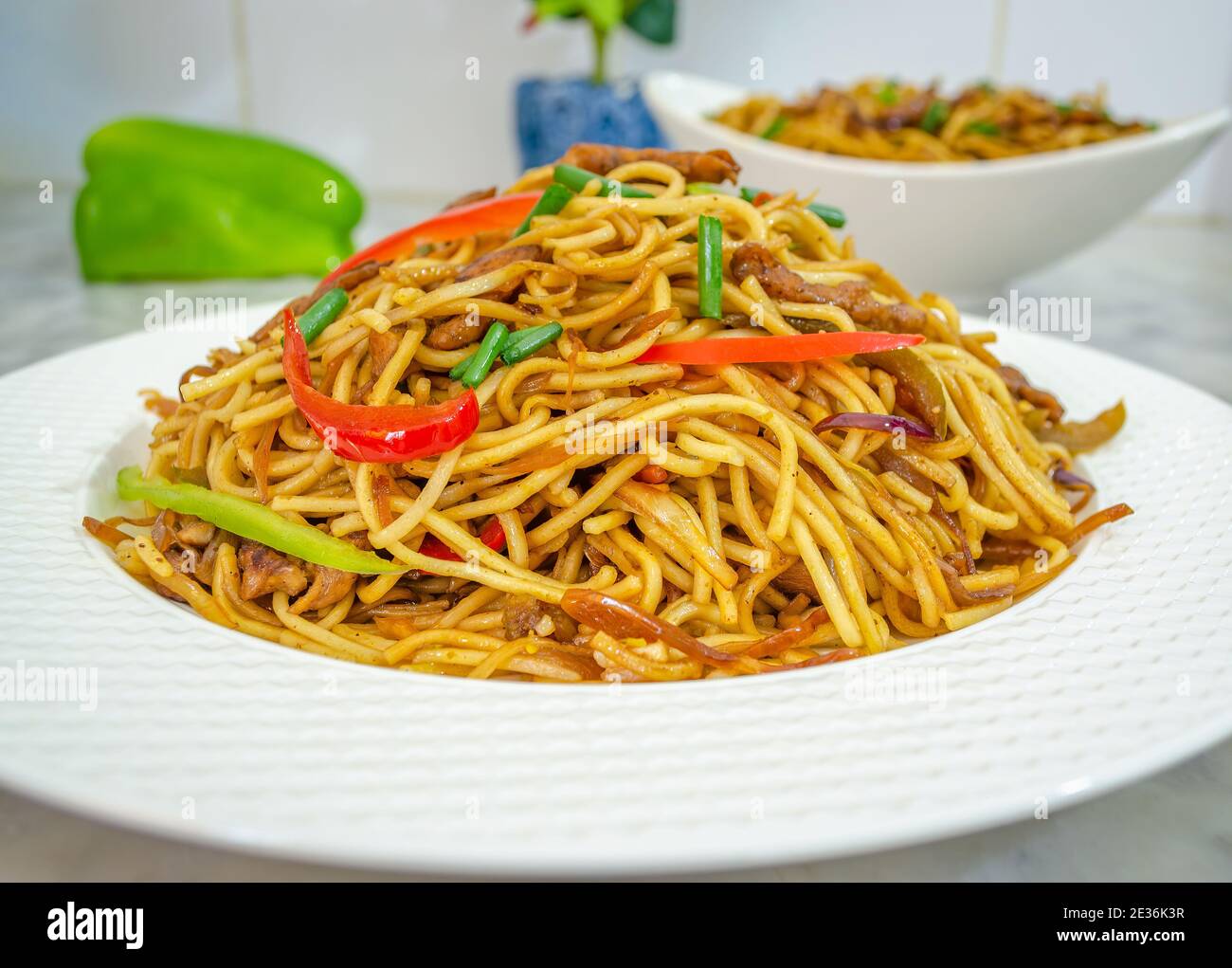 Closeup of beautifully arranged Chicken Noodles garnished with red and green bell peppers and spring onions Stock Photo