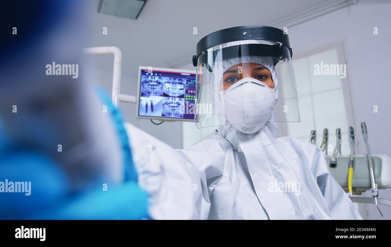 Patient pov of dentist in covid protectiv suit measuring temperature in
