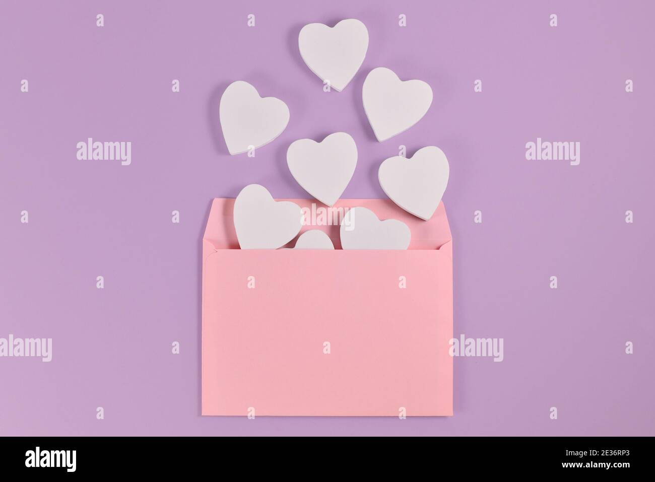 Love letter with pink envelope with white hearts spilling out on pastel colored violet background Stock Photo