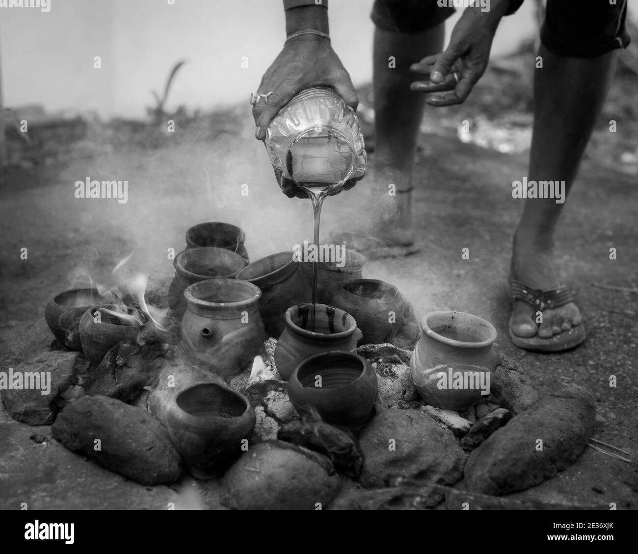 Black and white street photograph of a man pouring oil into fire lamps in India Stock Photo