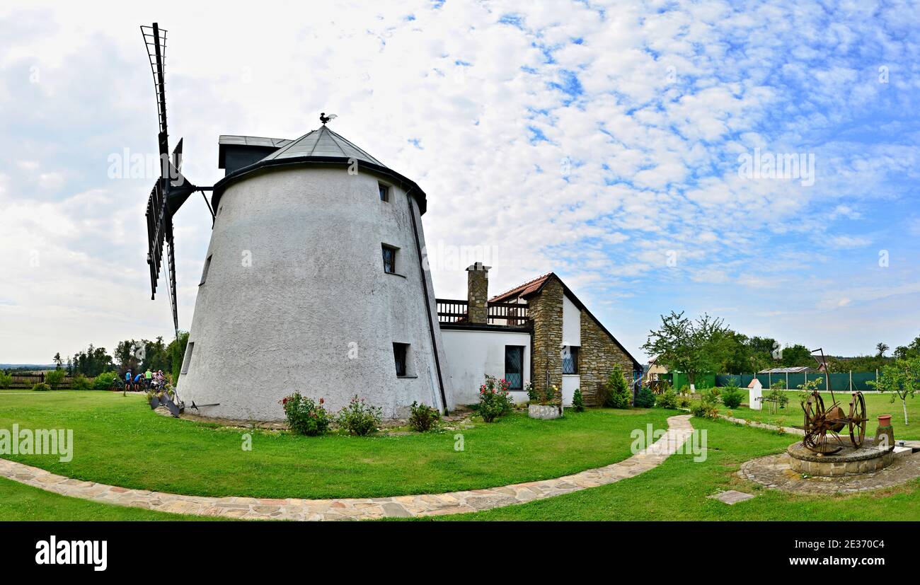 Windmill on green field with sky and clouds in background. Wide-angle panorama with a romantic view of a windmill on a summer sunny day. Stock Photo
