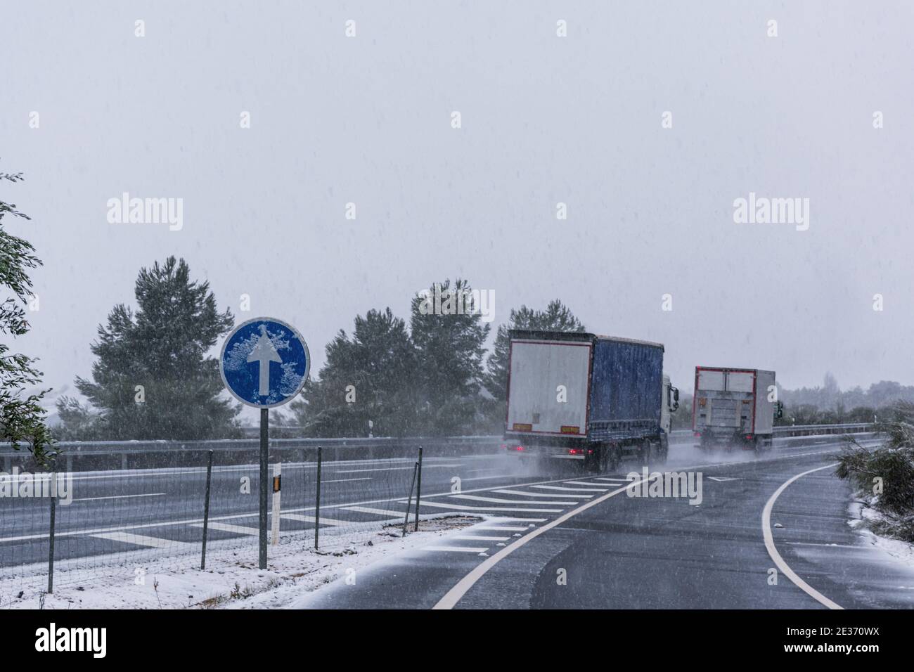 Two trucks driving with little safety distance on the highway on a day of adverse weather due to snowfall. Stock Photo
