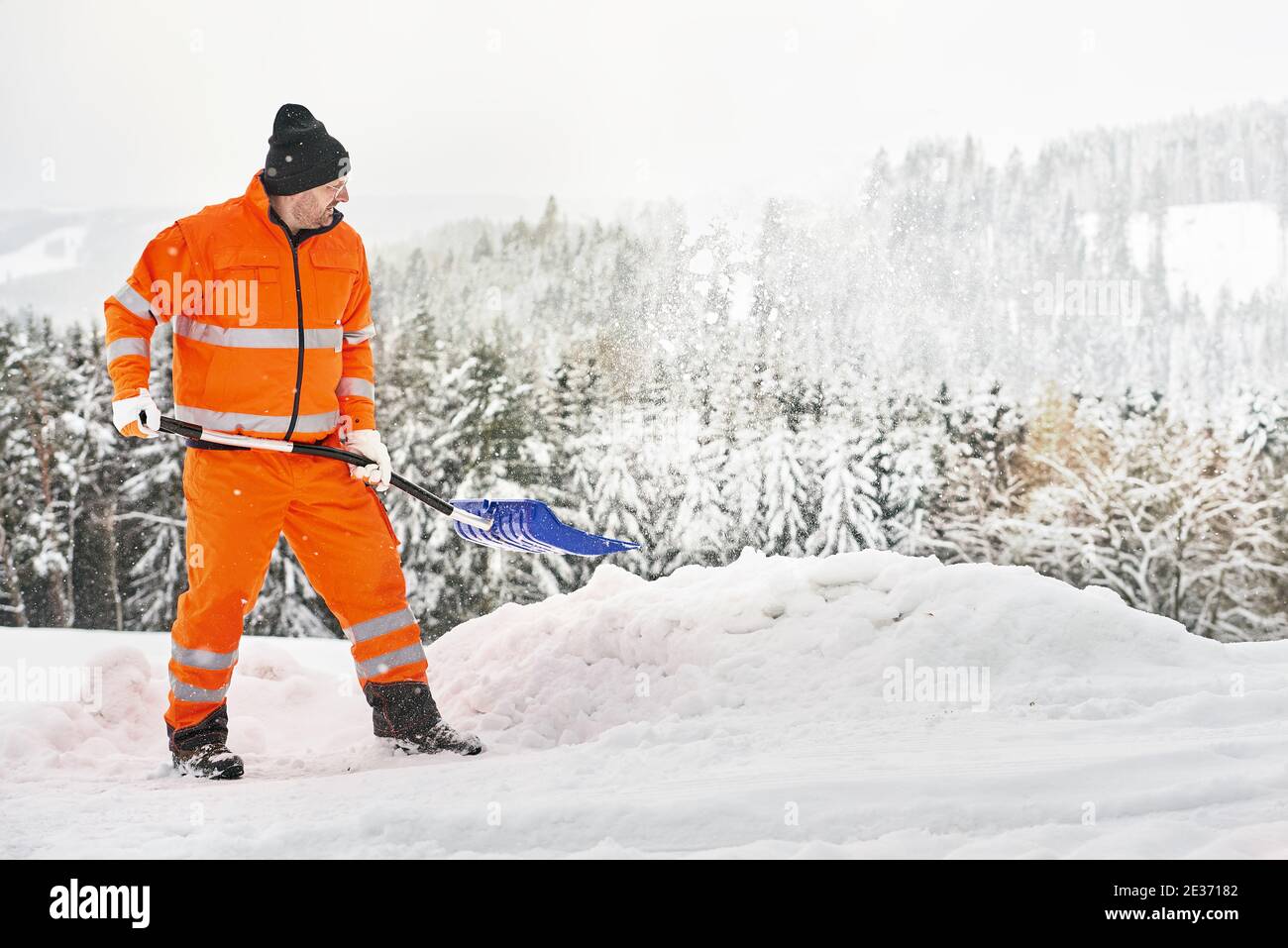 Communal service worker in uniform with a shovel clears snow in winter Stock Photo