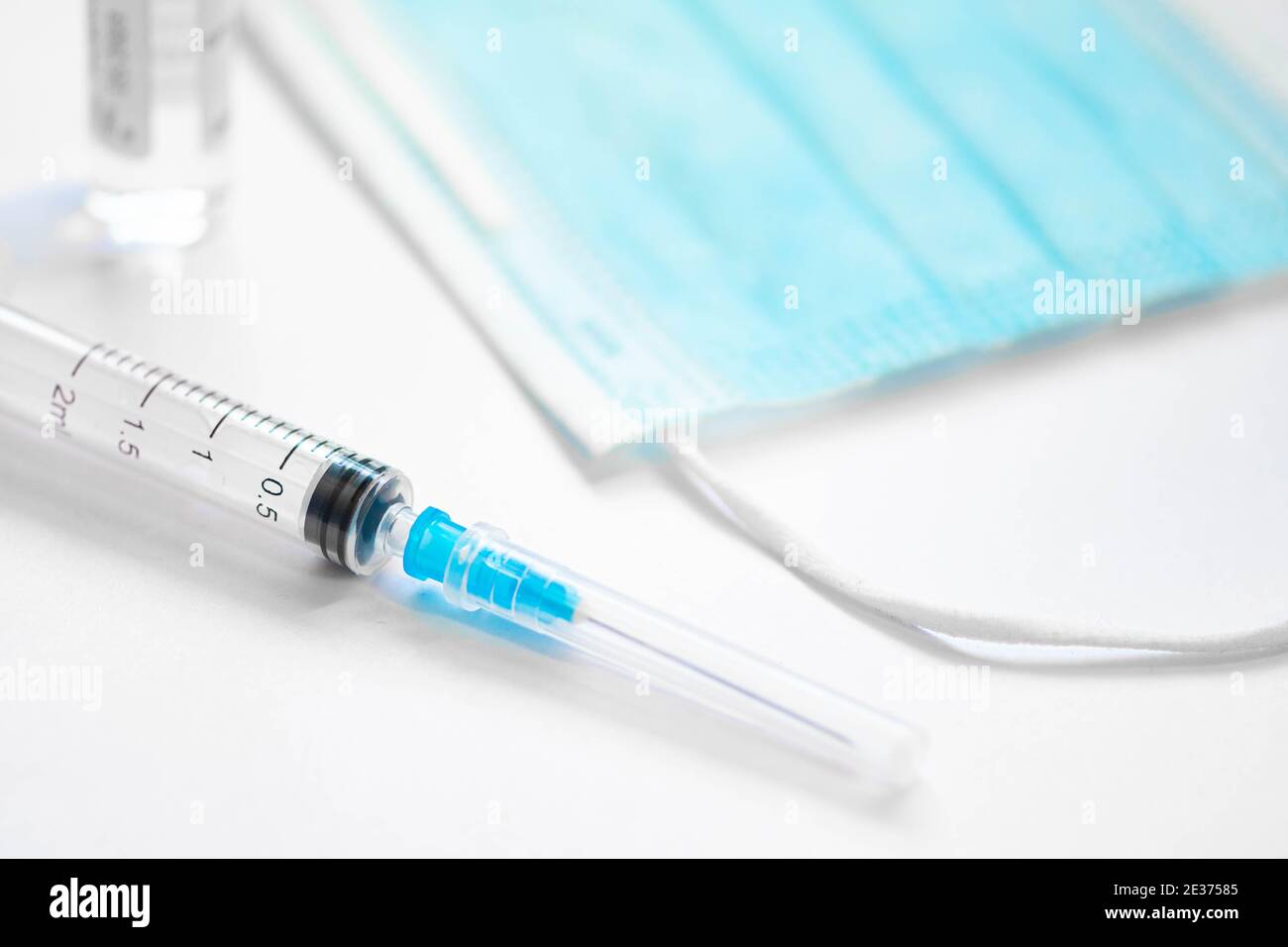 Syringe with needle, vial and surgical face mask on a white table ready to be used. Covid or Coronavirus vaccine background Stock Photo