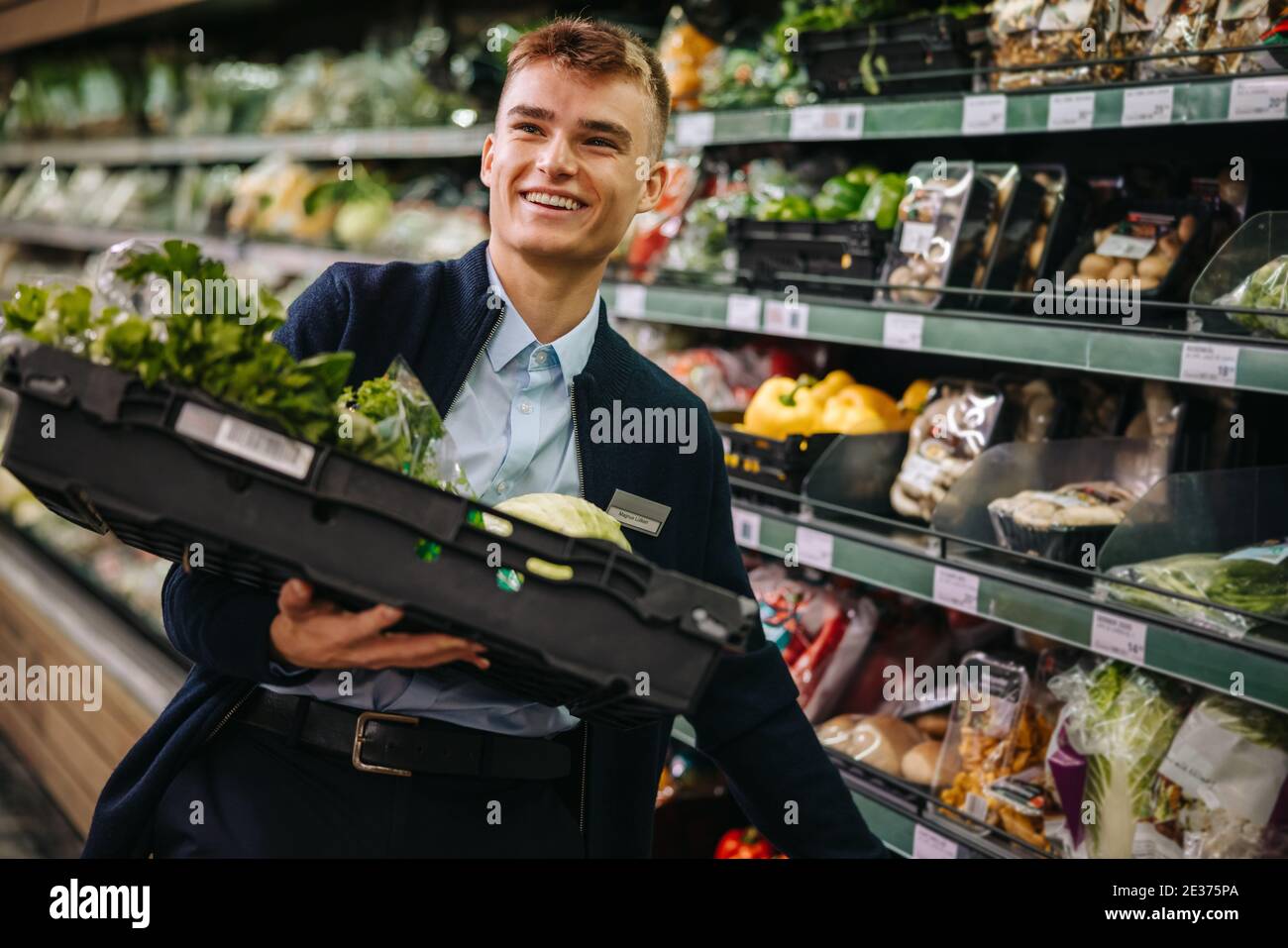 Man working in a supermarket restocking fresh fruit and vegetables in produce section. Young