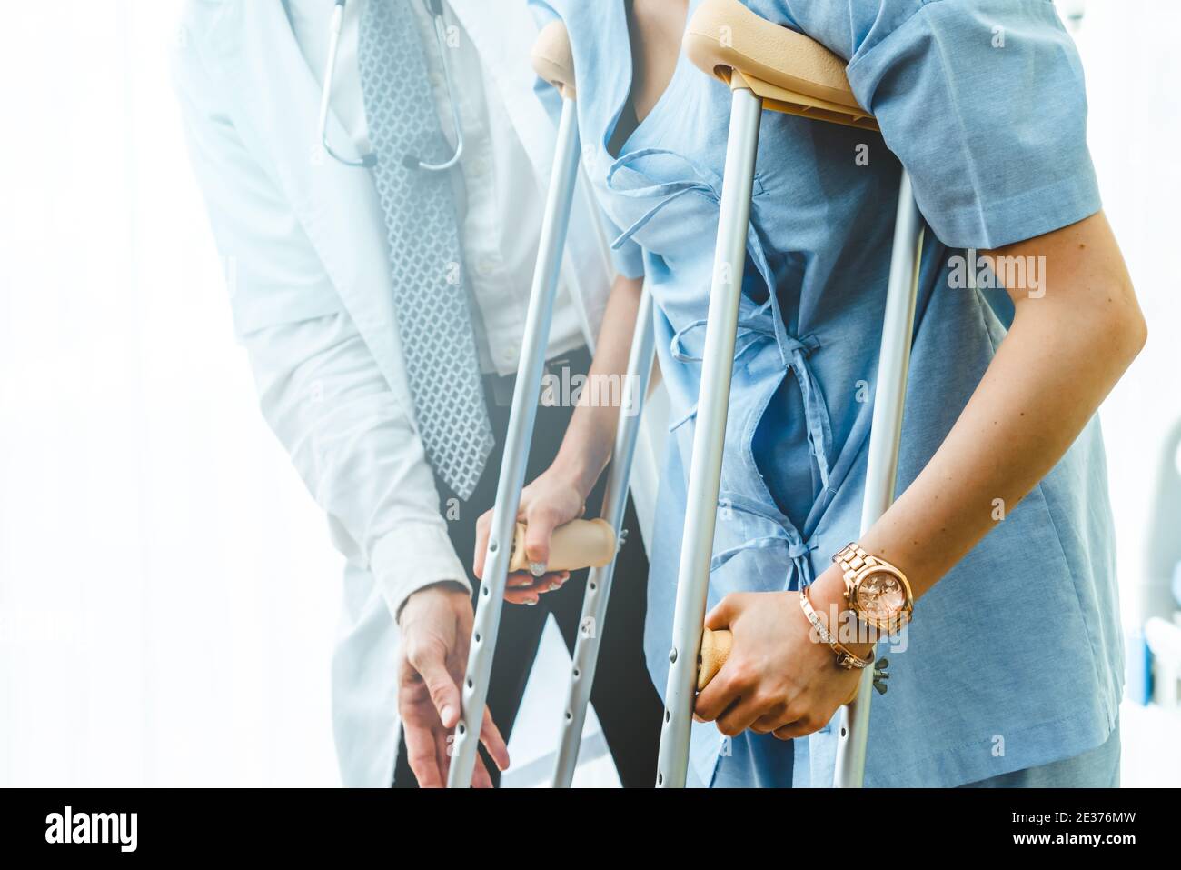 Doctor takes care of patient in crutch at hospital. Physical therapist and leg injury recovery