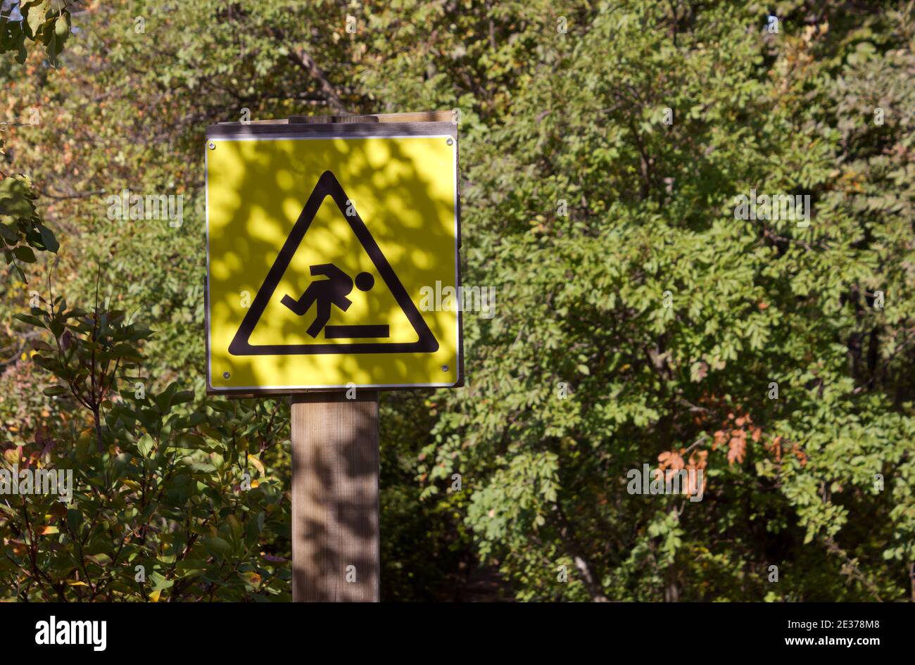 Yellow watch your step sign among lush vegetation along a nature trail Stock Photo