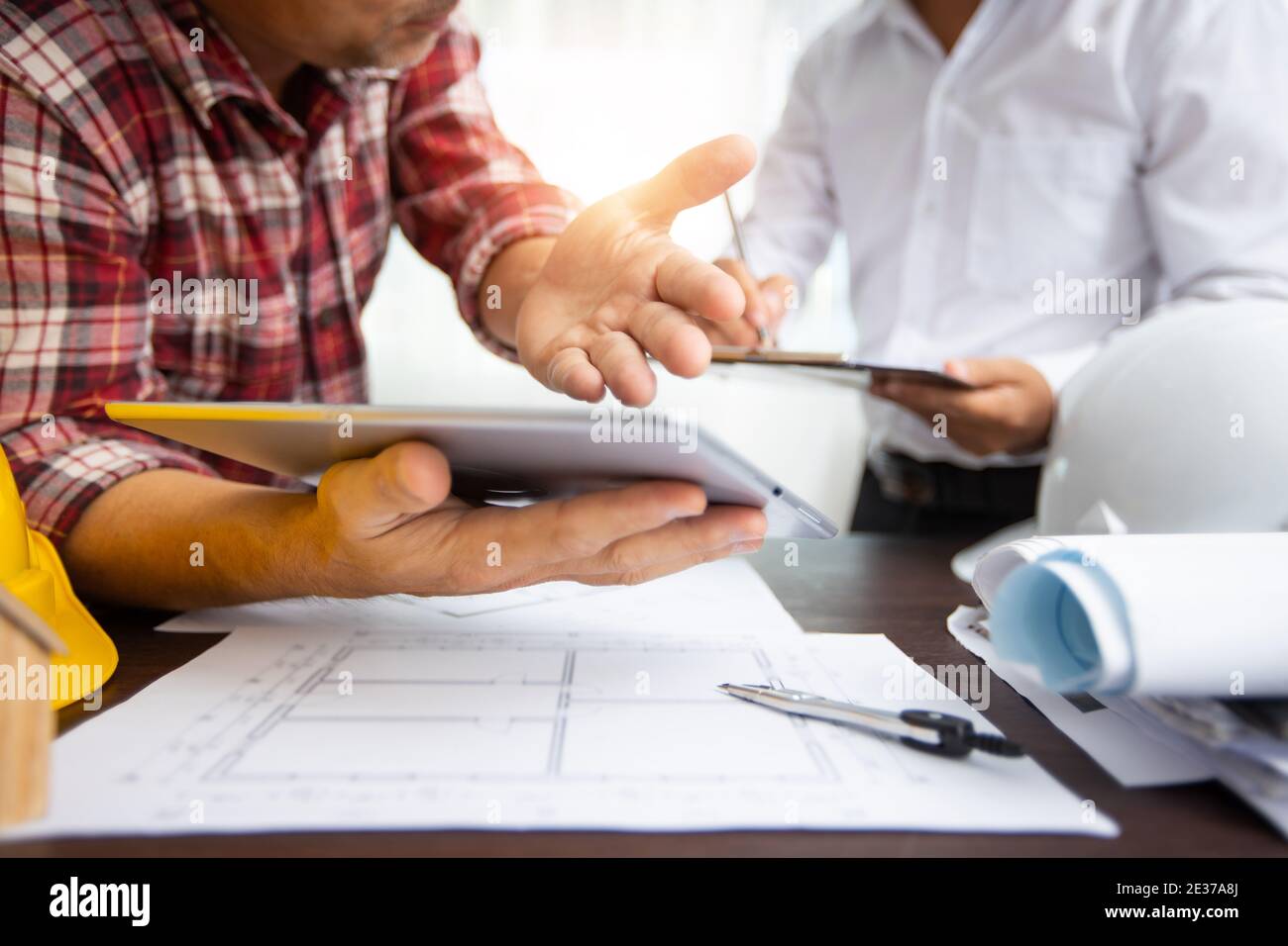 close up hand of engineer explaining project work on tablet and discussing about drawing blueprint as partner writing data on paper, architect meeting Stock Photo