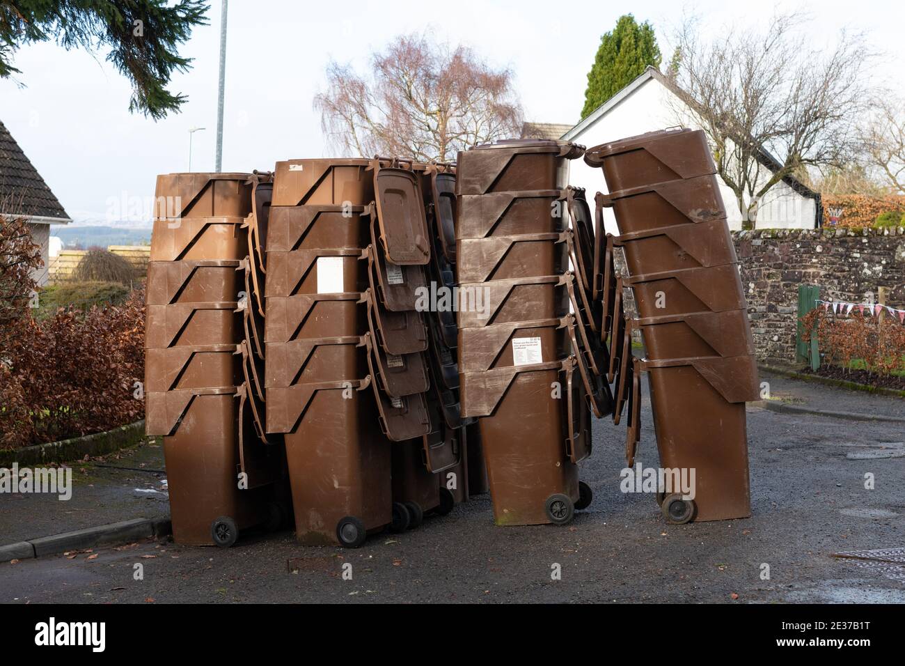 Brown domestic garden waste bins stacked at the side of the road for