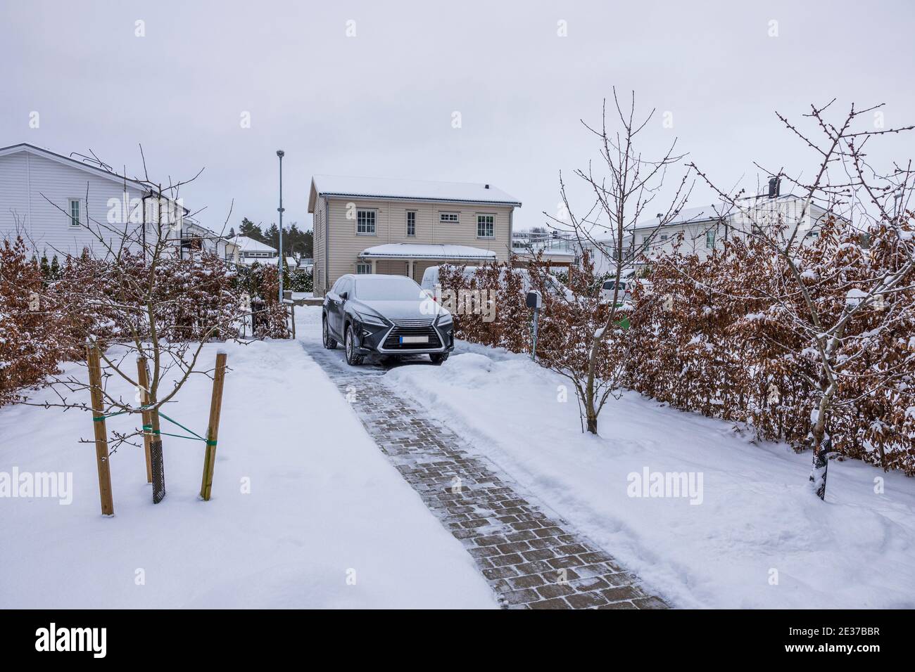 View of winter landscape of private area. Car, trees and bushes covered with snow. Beautiful white villas on background. Stock Photo