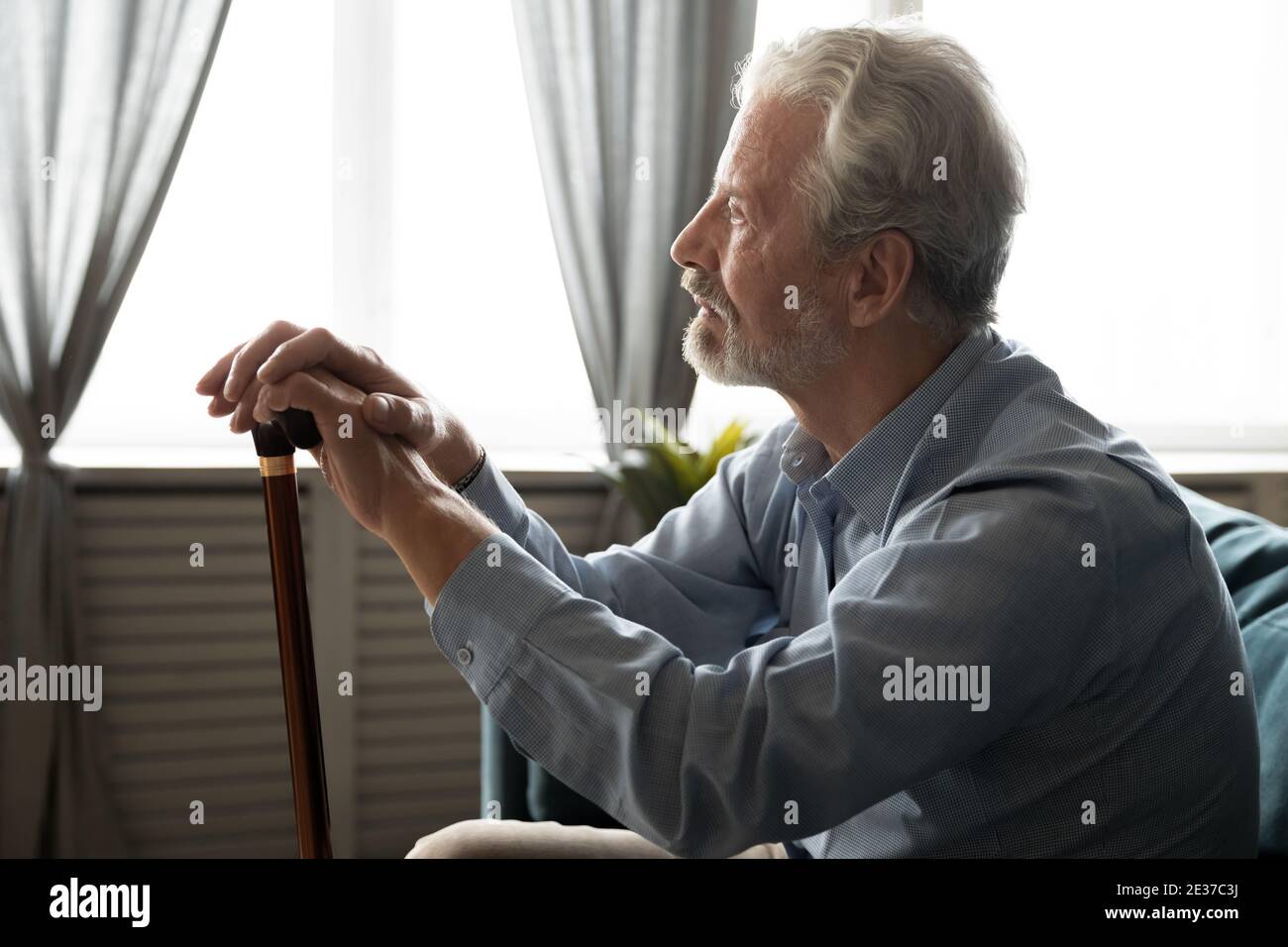 Pensive stressed middle aged disabled old man sitting on sofa. Stock Photo