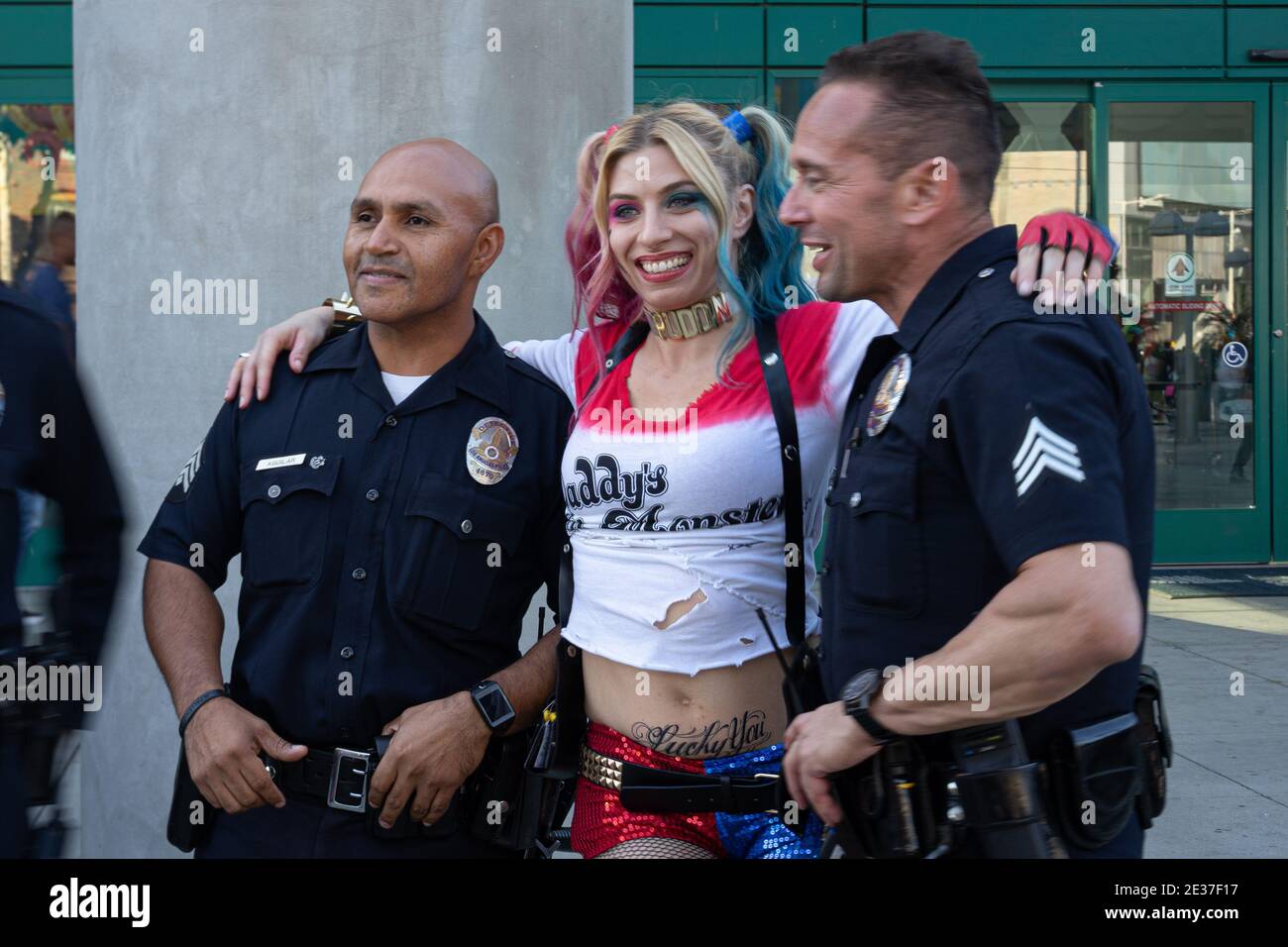 A cosplayer dressed as Harley Quinn with her hands on the shoulders of two smiling uniformed policemen, Comicon LA, California 2019 Stock Photo
