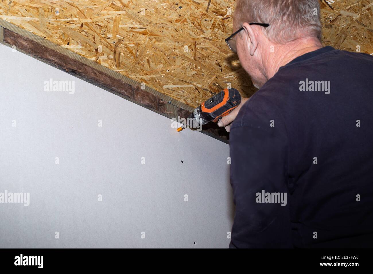 A man screws a drywall sheet to metal profiles with a screwdriver. Home renovation. Wall covering. Stock Photo