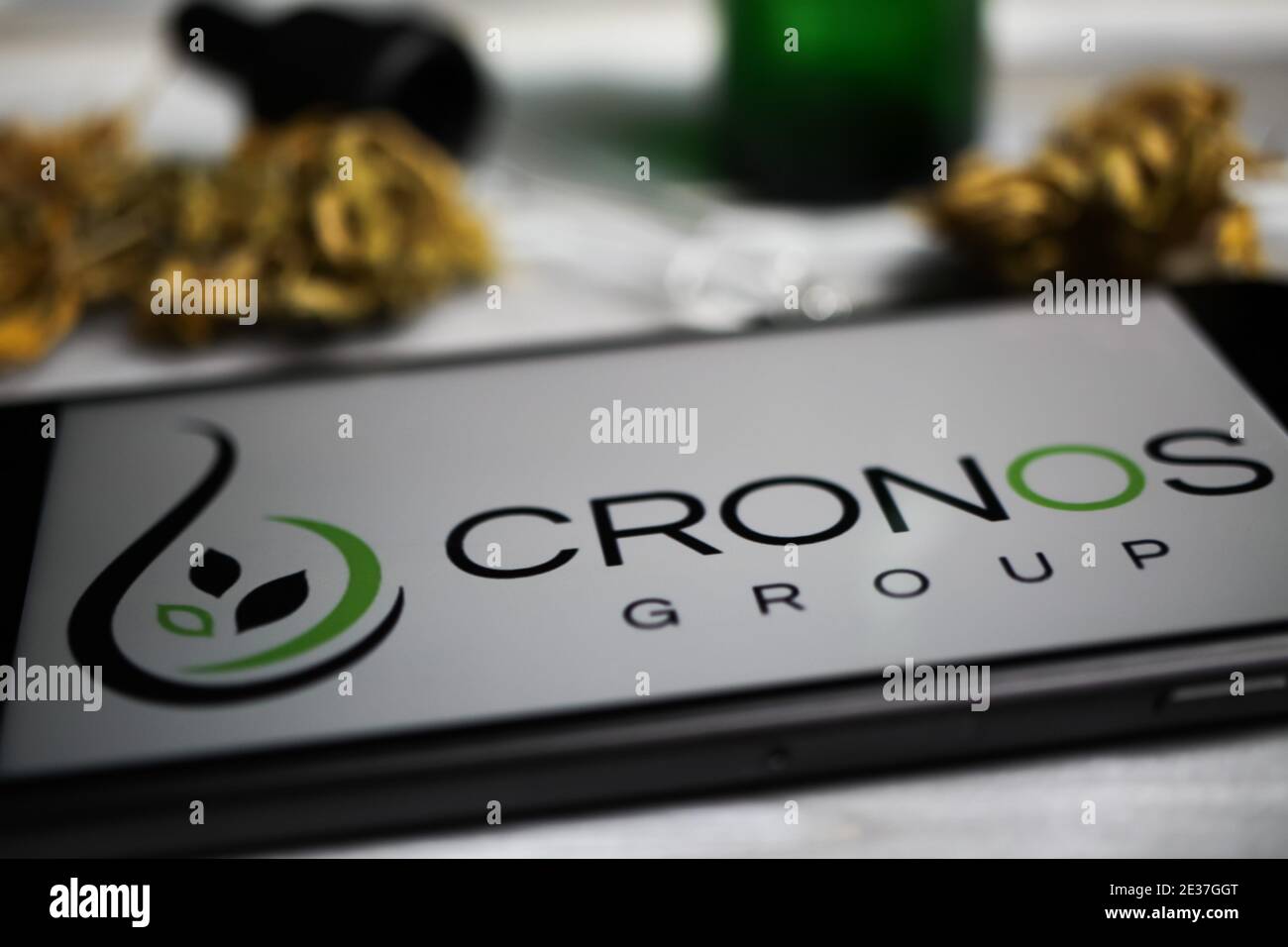 Viersen, Germany - January 9. 2021: Closeup of mobile phone screen with logo lettering of cannabinoid company cronos group, blurred marijuana and pipe Stock Photo