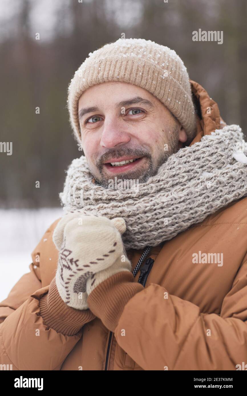 Vertical portrait of bearded mature man in winter outdoors wearing knit hat and jacket while smiling at camera covered in snow Stock Photo