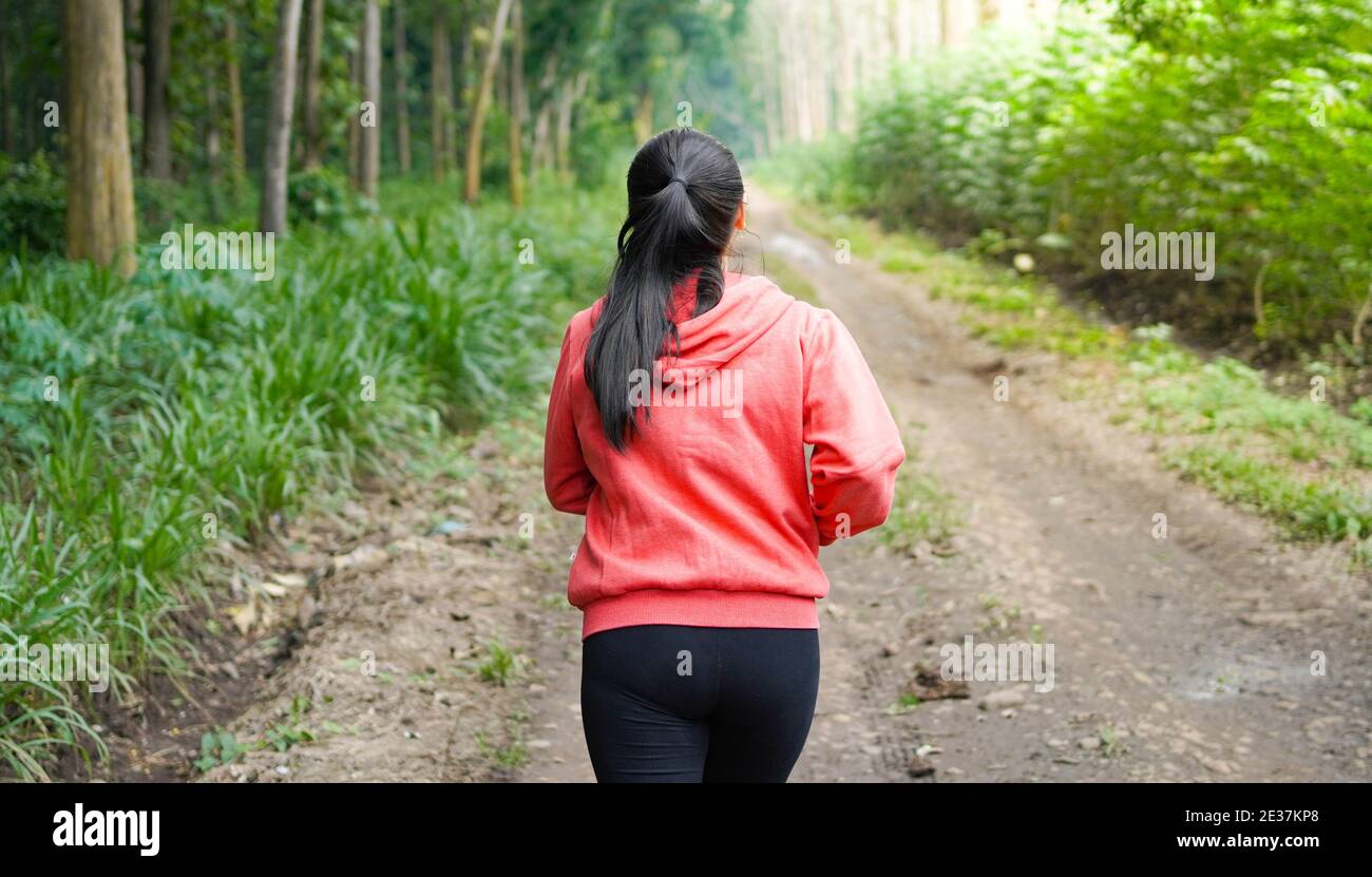 Asian woman running in forest wearing jacket Stock Photo