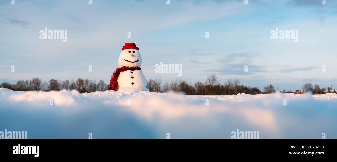 Funny snowman in stylish red hat and red scalf on snowy field. Panoramical photo ideal for site head mockup Stock Photo