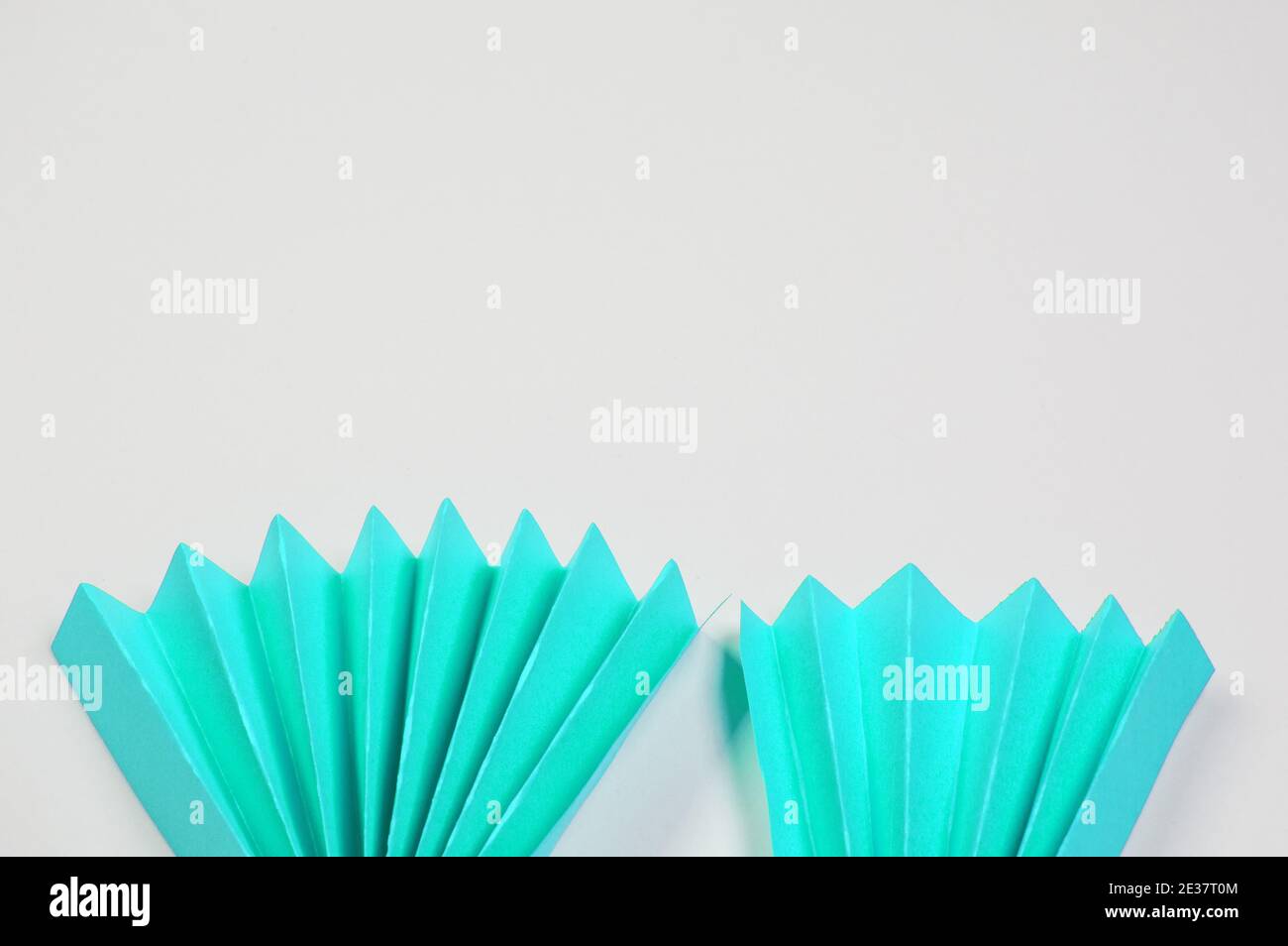 Two light blue origami paper fans located on the bottom edge on a white