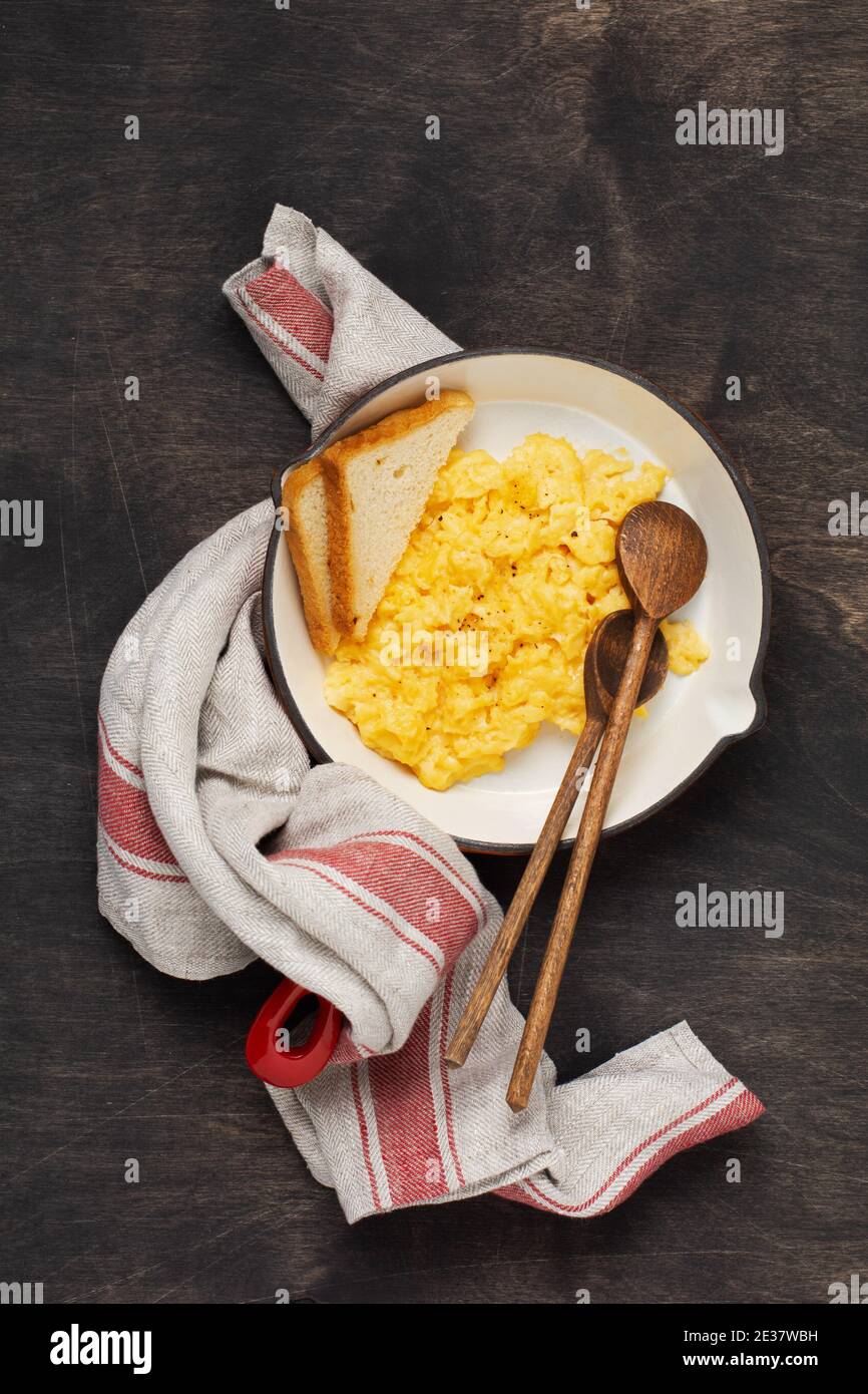 Scrambled eggs for breakfast on red old frying pan, dark wooden table ...