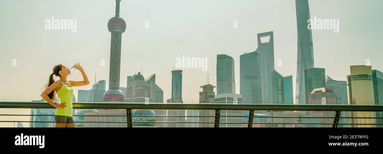 Fit athlete Asian girl drinking water at Shanghai skyline fitness woman thirsty on sunny day, China panoramic banner. Health and sports lifestyle. Stock Photo