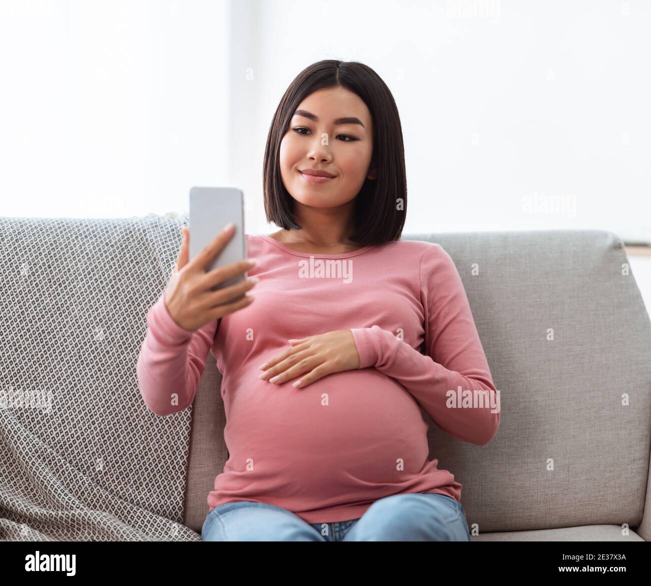Pregnant Chinese Lady Using Phone Making Selfie Sitting At Home Stock Photo