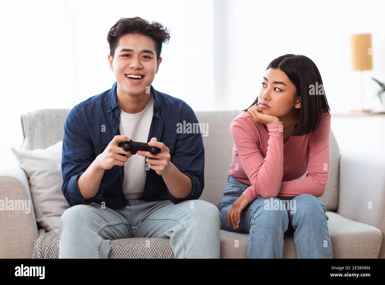 Displeased Japanese Girlfriend Looking At Boyfriend Playing Game At Home Stock Photo