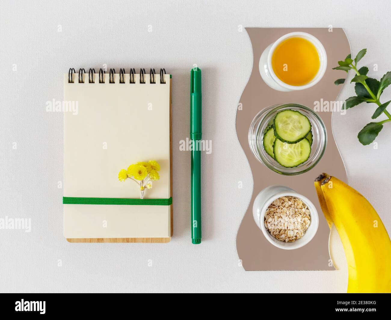 Natural ingredients for the preparation of home skin care. Flat lay with cucumber, banana, oatmeal and oil for homemade beauty products with notepad o Stock Photo