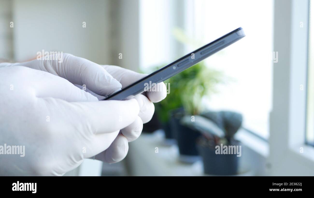 Image with Doctor Hands Wearing Protective Gloves Browsing Internet Connection and Sending an Email Using a Smartphone Stock Photo