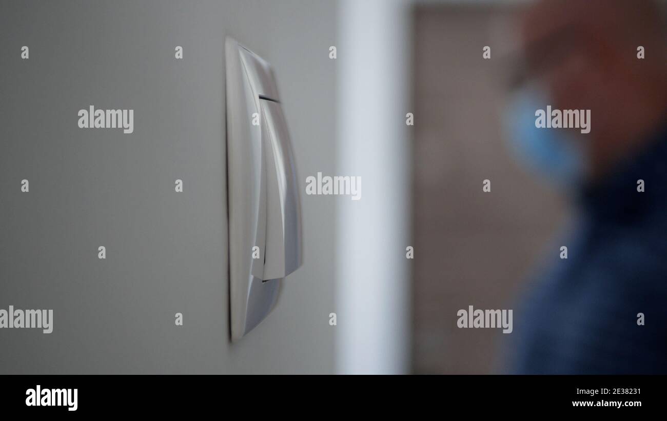 A Light Switch on the Wall and a Blurred Person in Background Wearing Medical Face Mask Entering in the Office Stock Photo