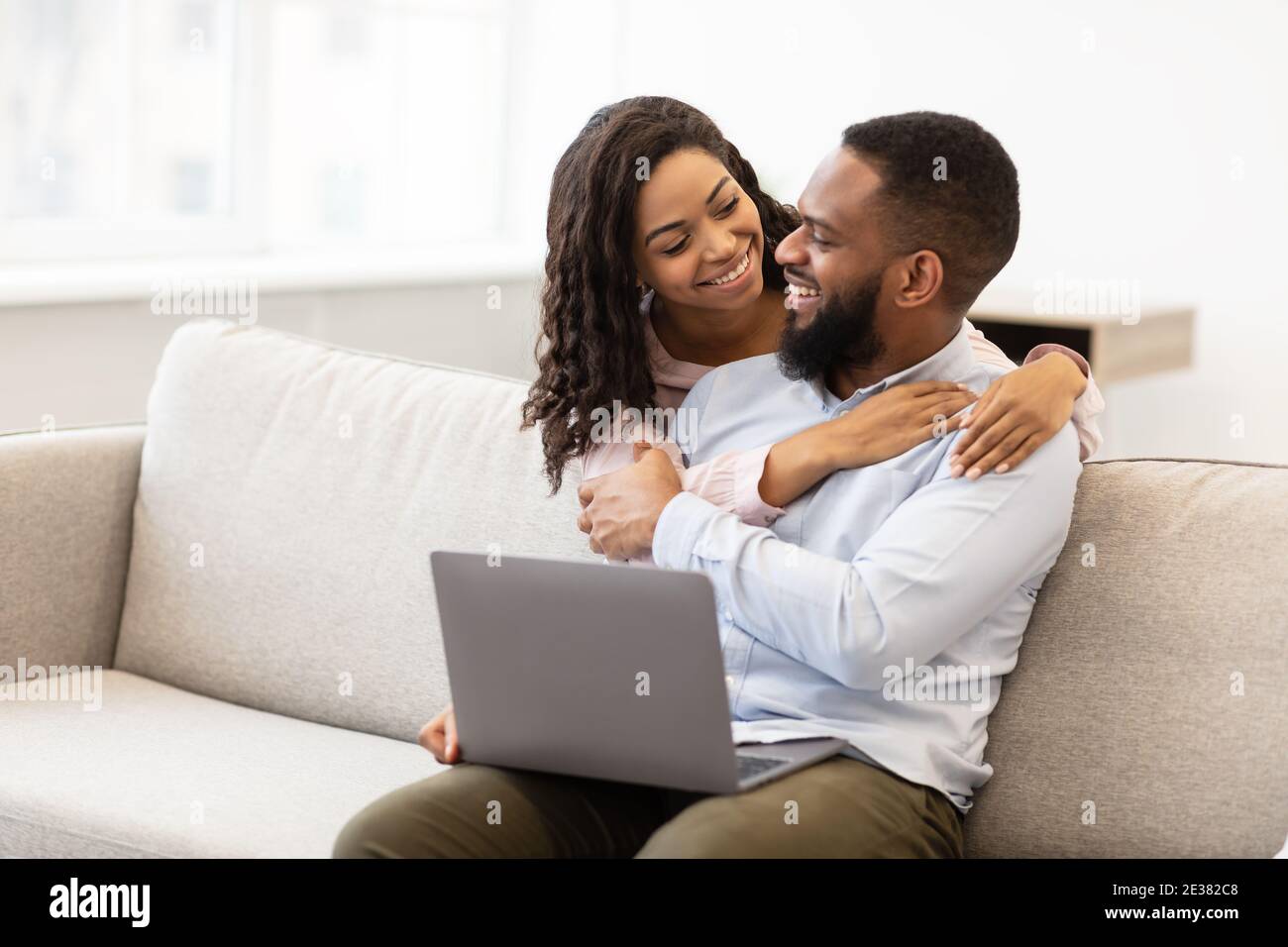 African american couple sitting on couch, using laptop, cuddling Stock ...