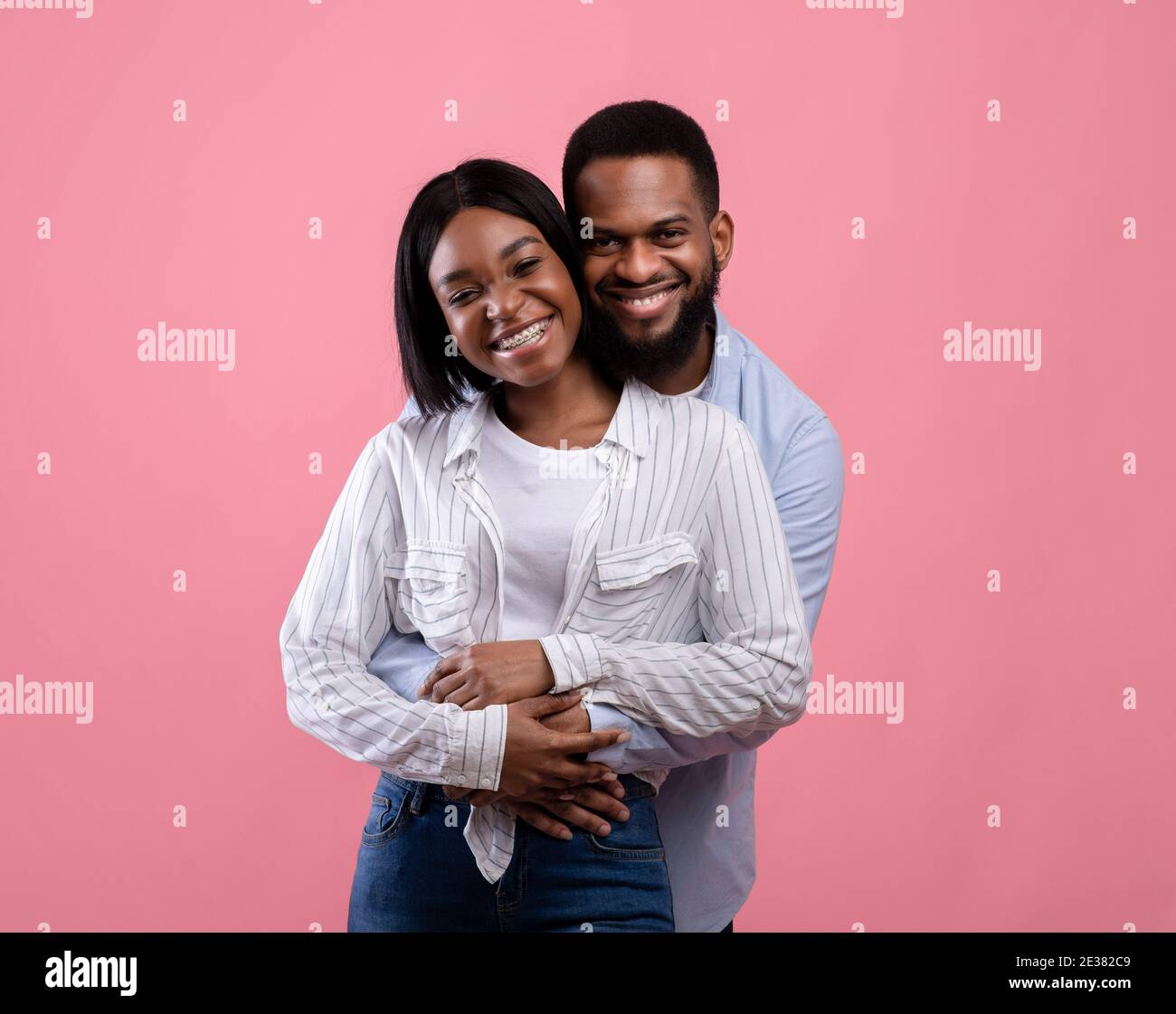 Portrait of lovely African American couple hugging and cuddling, feeling happy on pink background. Valentine's Day Stock Photo