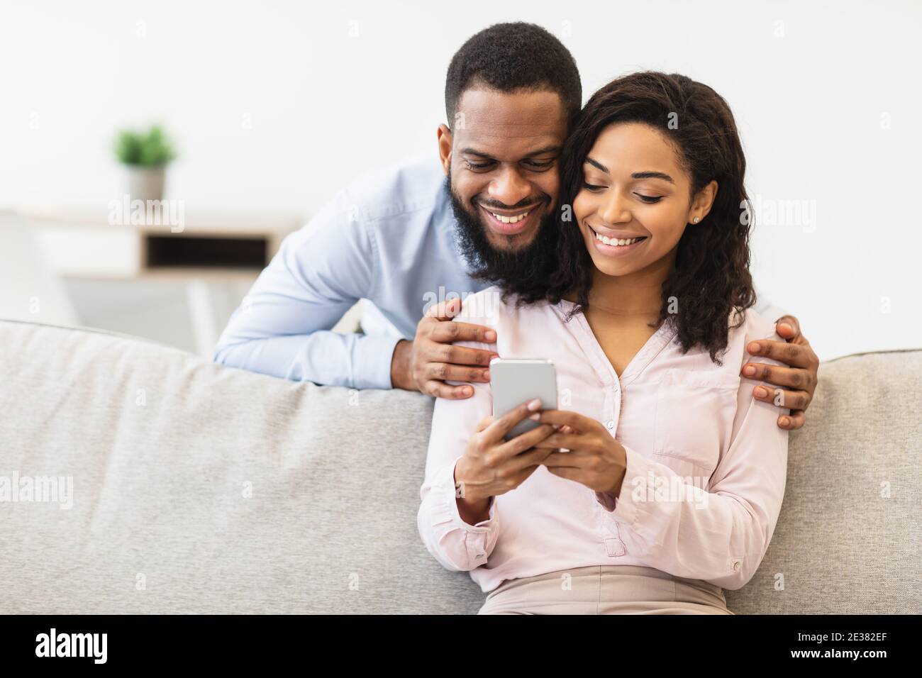 African american couple sitting on couch, using cellphone Stock Photo ...