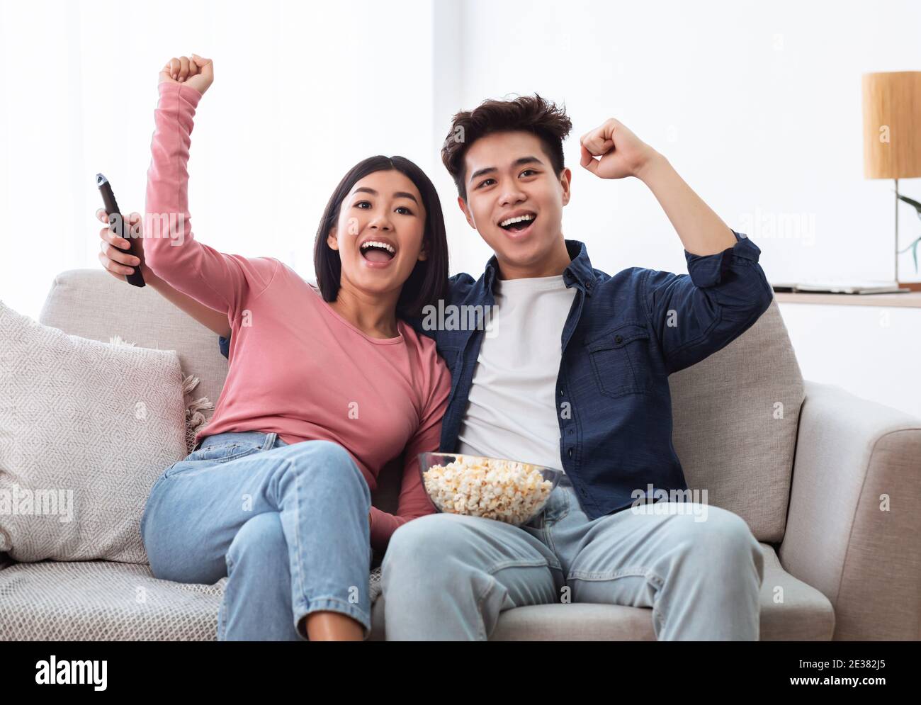 Excited Chinese Couple Watching TV Shaking Fists In Living Room Stock Photo
