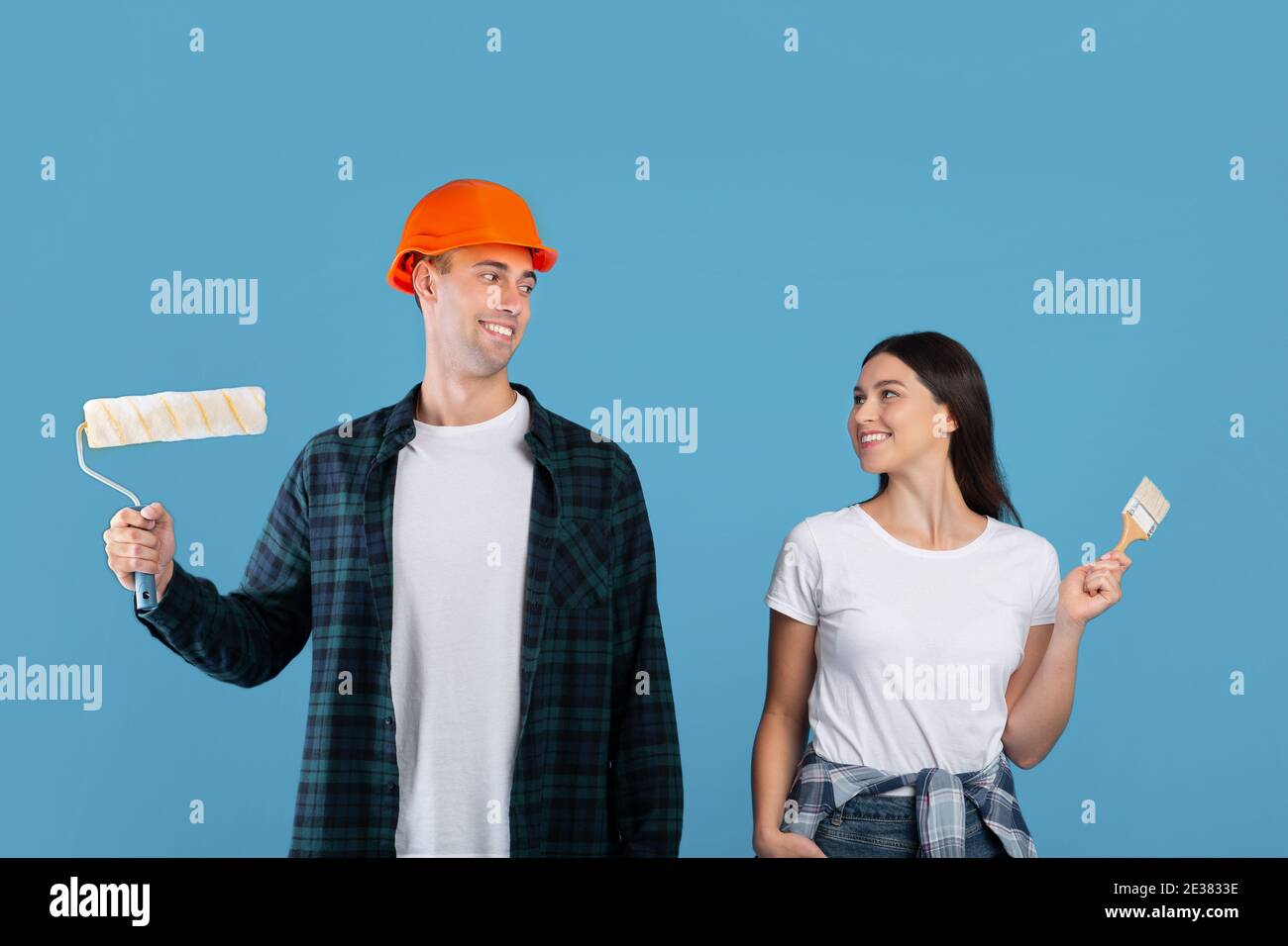 Happy Young Couple With Painting Tools In Hands Posing Over Blue Background Stock Photo