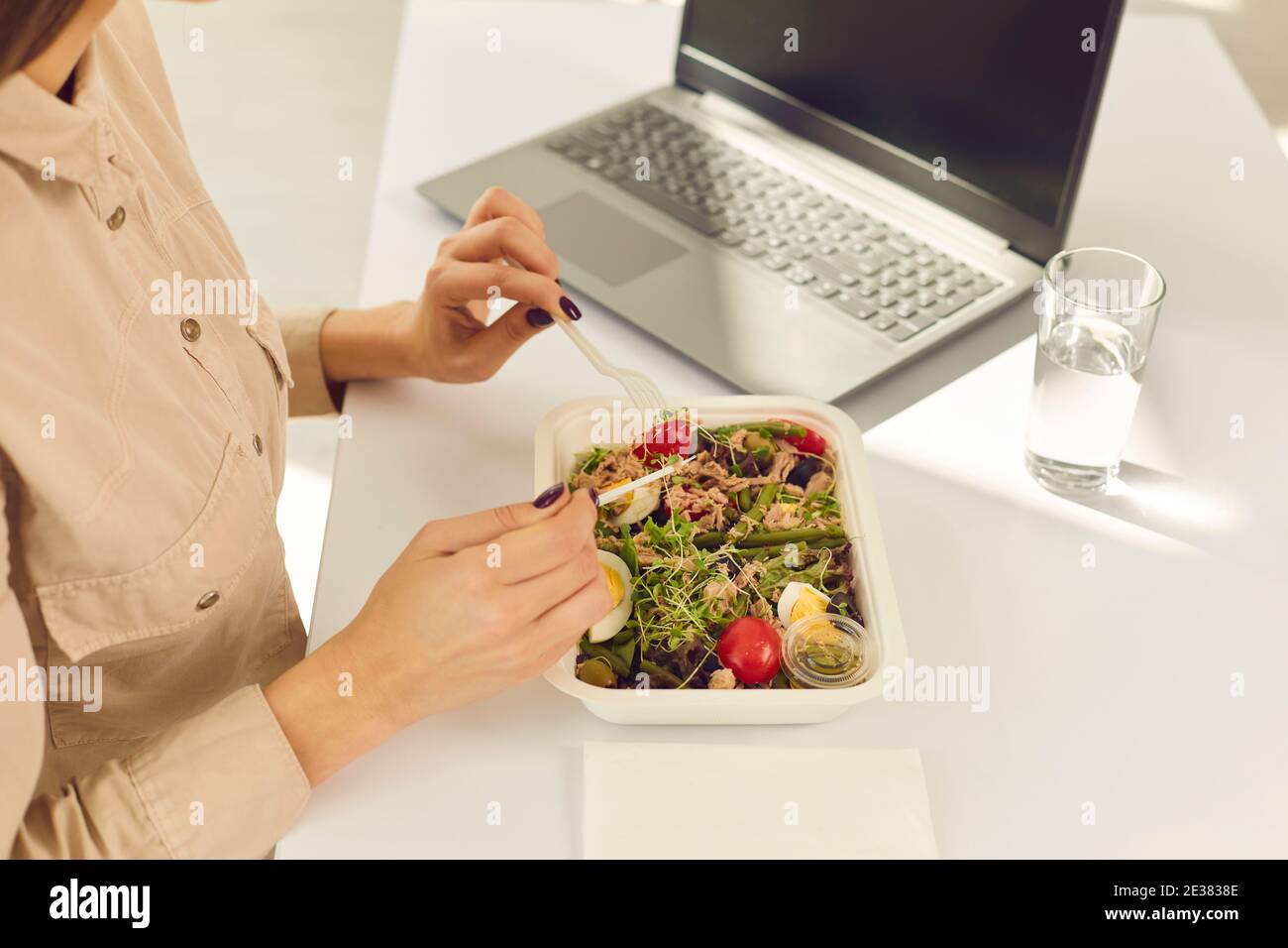 Woman office worker sitting at desk with laptop and water and enjoying healthy boxed food order Stock Photo