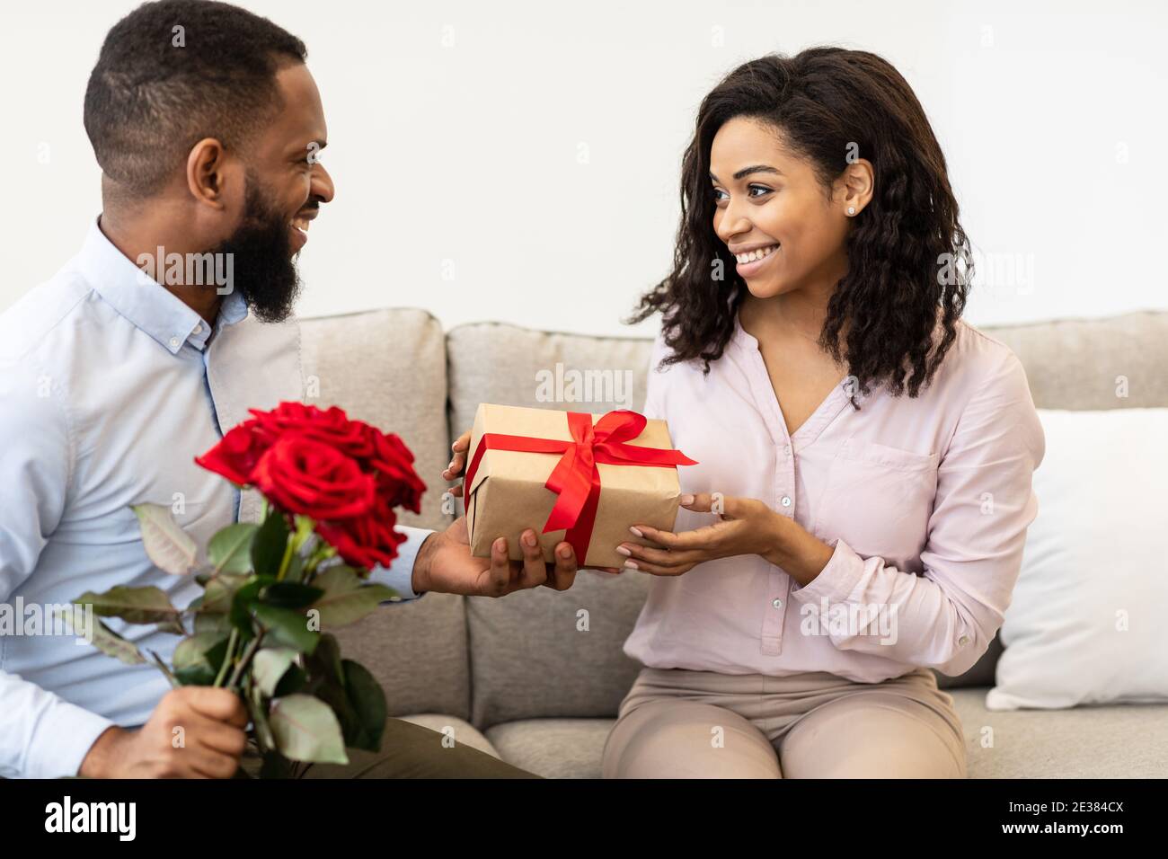 Happy black guy giving red roses and box to woman Stock Photo Alamy