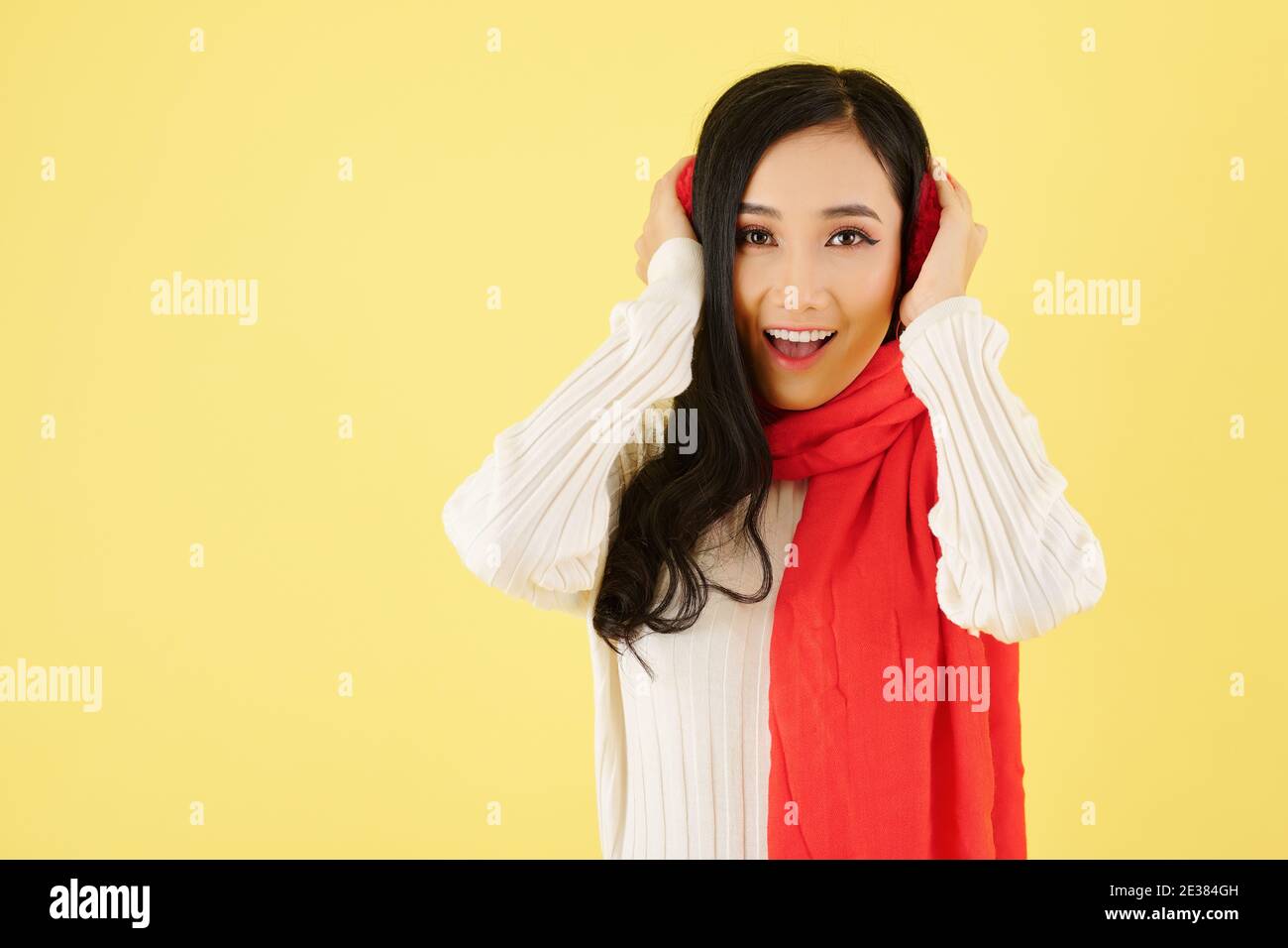 Portrait of excited young Asian woman wearing ear muffs and warm wool scarf for winter day Stock Photo