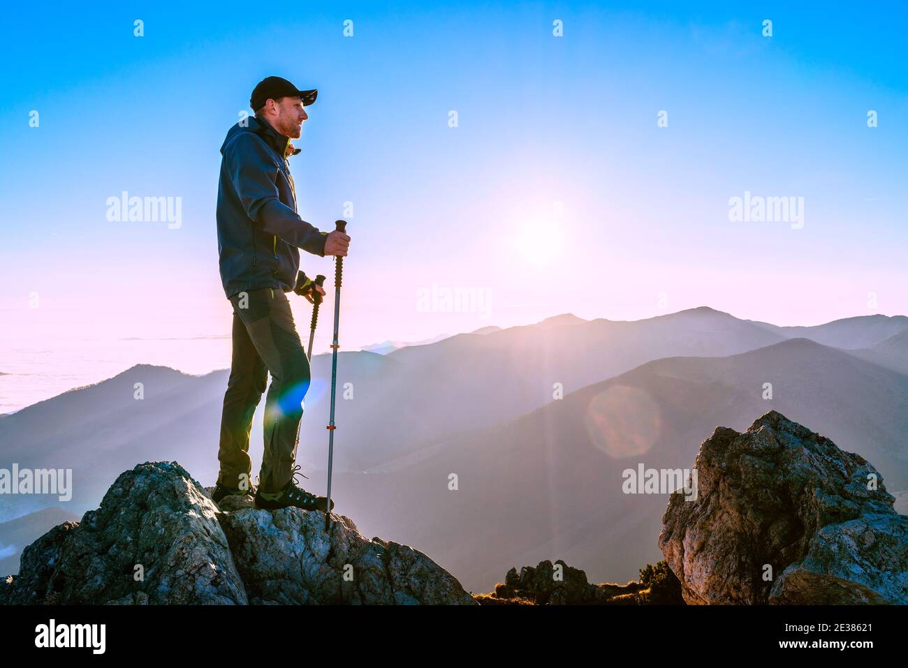 Hiker Man standing with trekking poles on a cliff edge and looking at Tatra mountains valley covered with clouds. Successful Velky Rozsutec 1610m summ Stock Photo