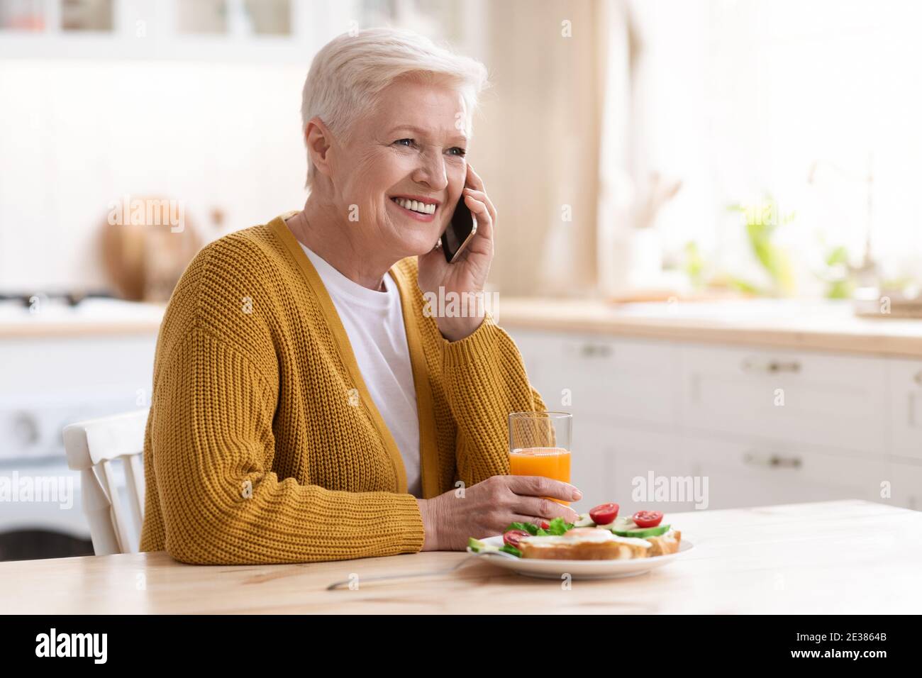 Cheerful grandmother having phone call while eating at home Stock Photo