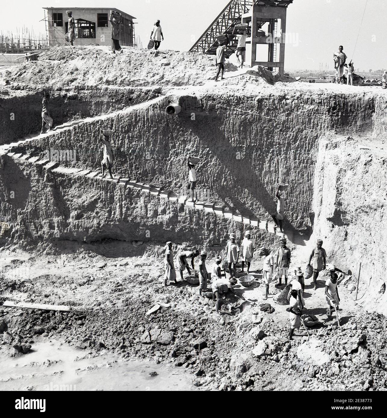 1950s, historical, indian labourers in turbans and in barefeet carrying  baskets of earth dug from a deep pit, perhaps for foundations, up a  staircase cleverly dug out at the side of the