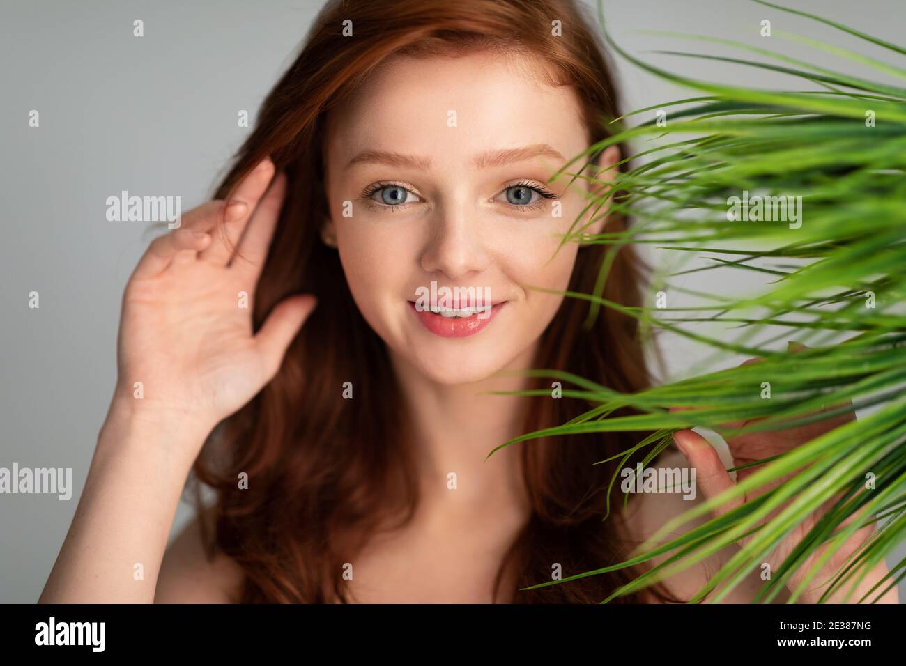 Ginger-Haired Young Woman Posing With Green Plant Leaves, Gray Background Stock Photo