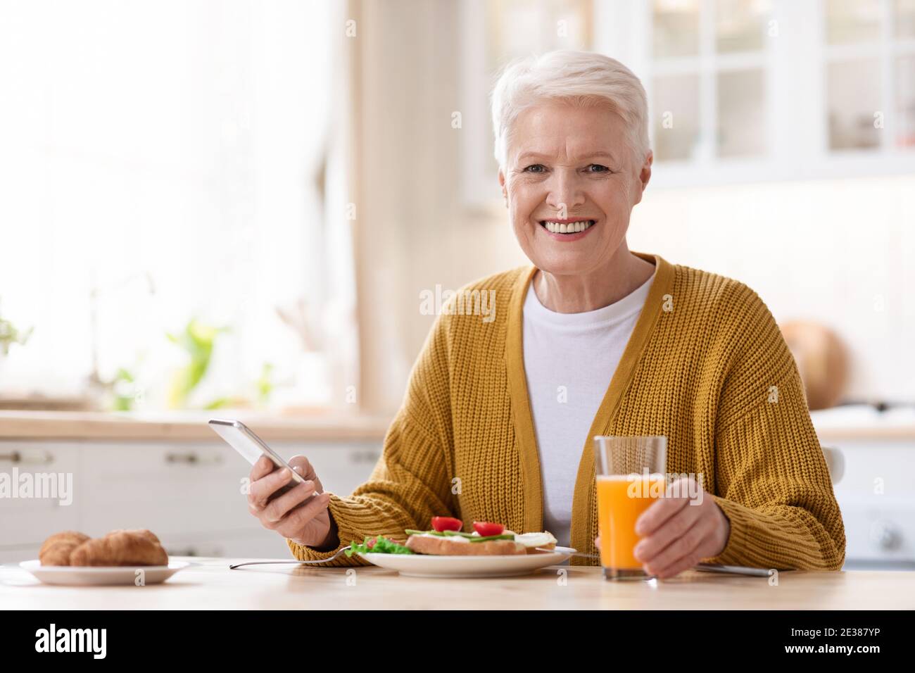 Smiling old lady using mobile phone while having lunch Stock Photo