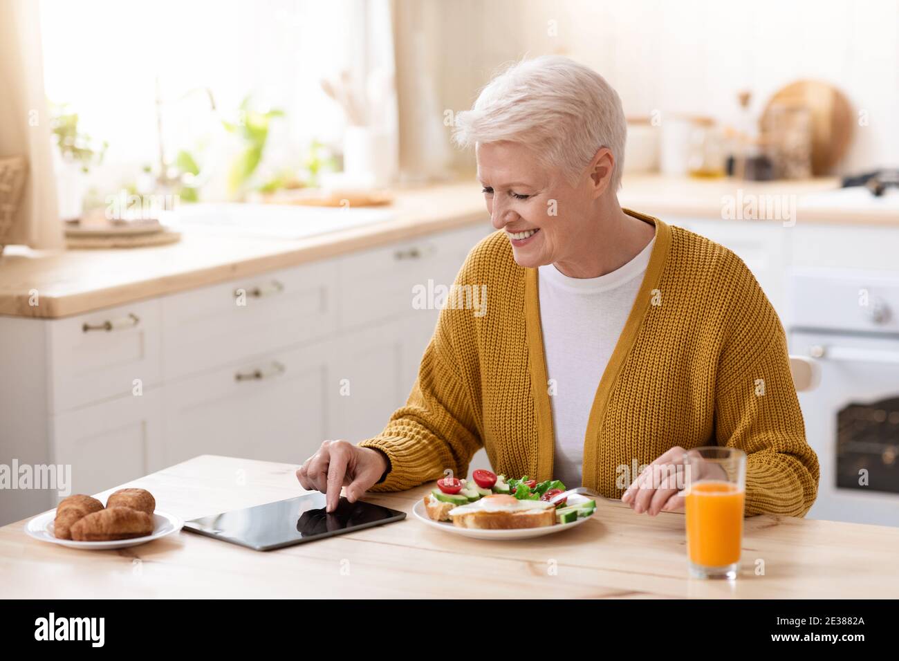 Smiling old lady using digital tablet while having lunch Stock Photo