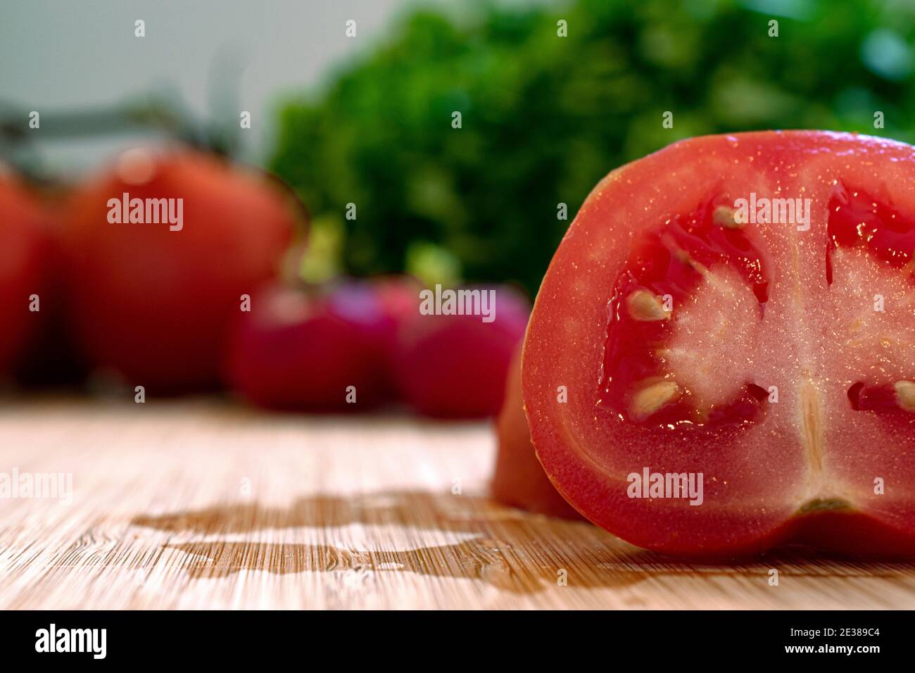 Close up of a tomato freshly cut in half arranged among healthy green lettuce and radishes Stock Photo