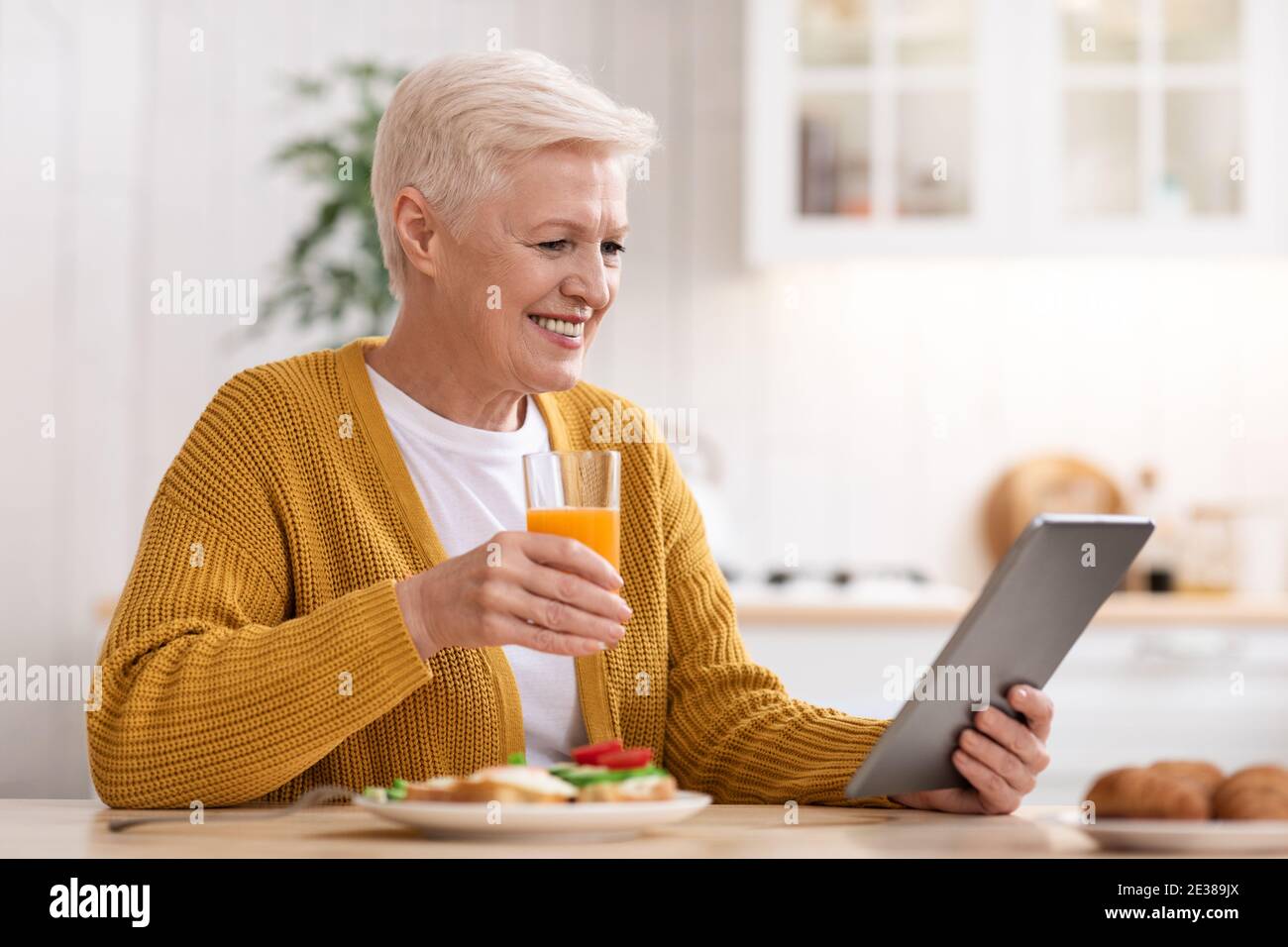 Joyful old woman eating healthy food and using digital tablet Stock Photo