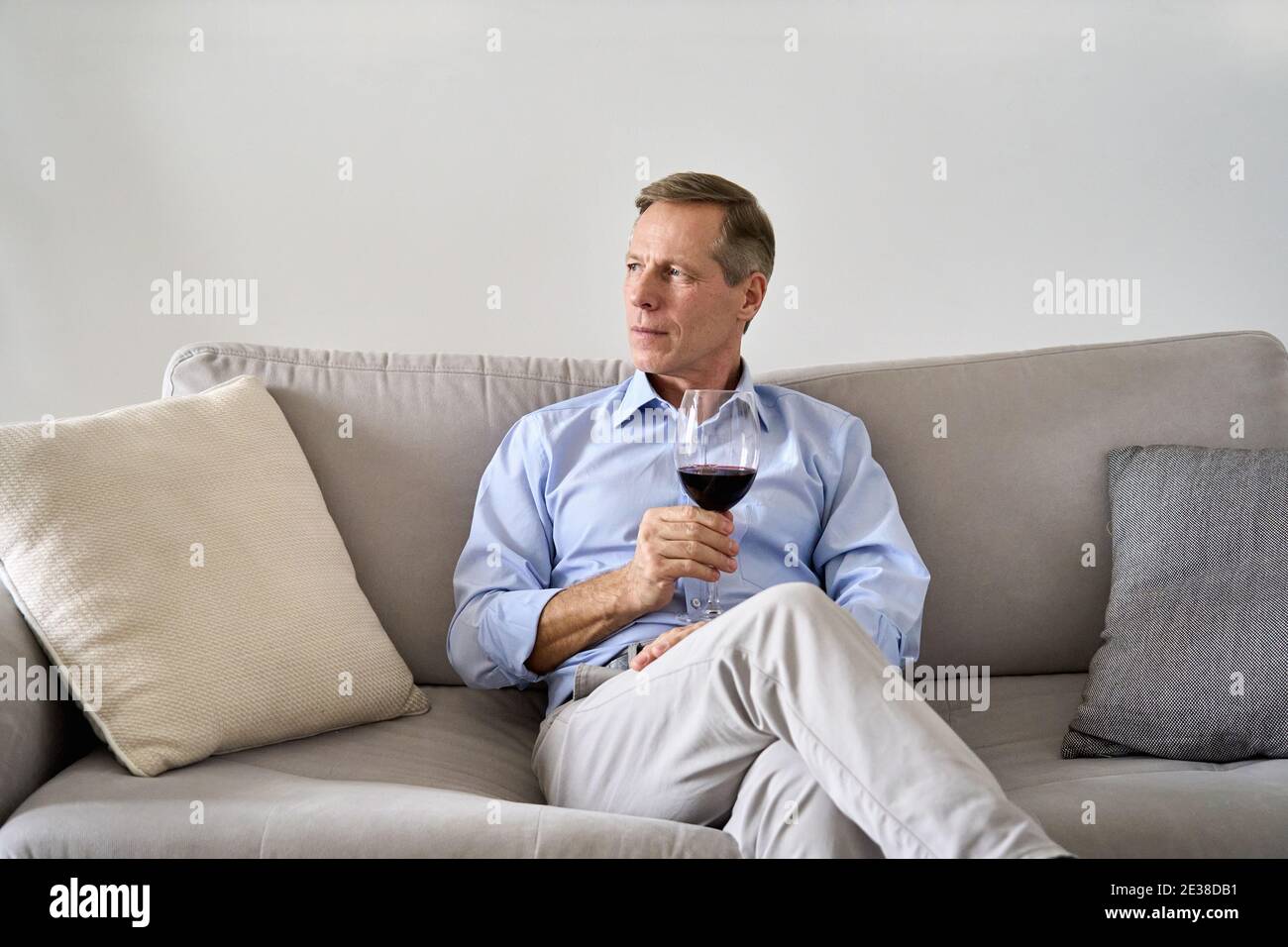 Relaxed old retired single man drinking wine relaxing on sofa at home. Stock Photo