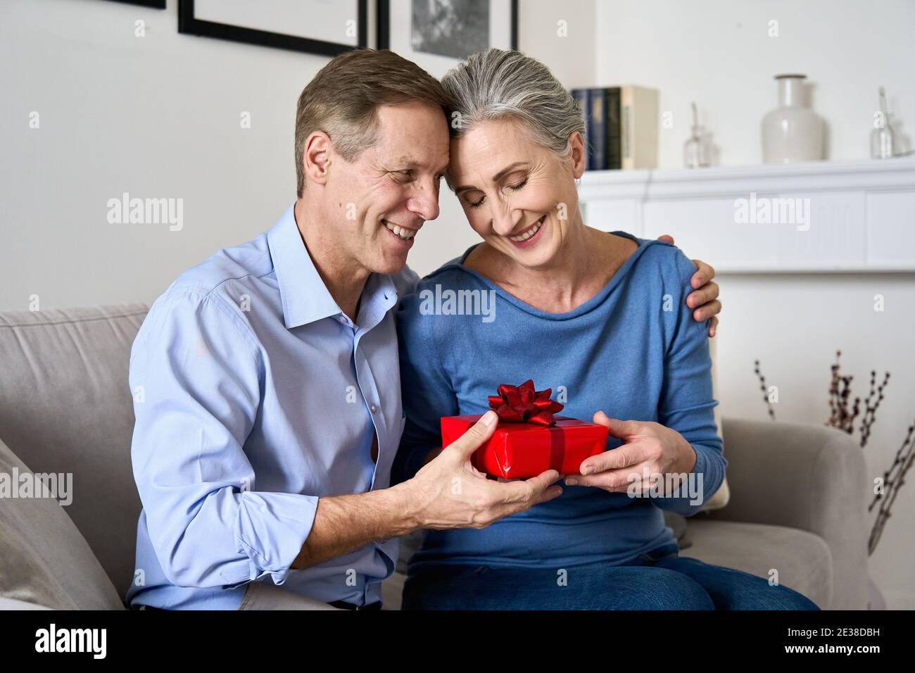 Happy old husband giving red gift box to wife making present on Valentines day. Stock Photo