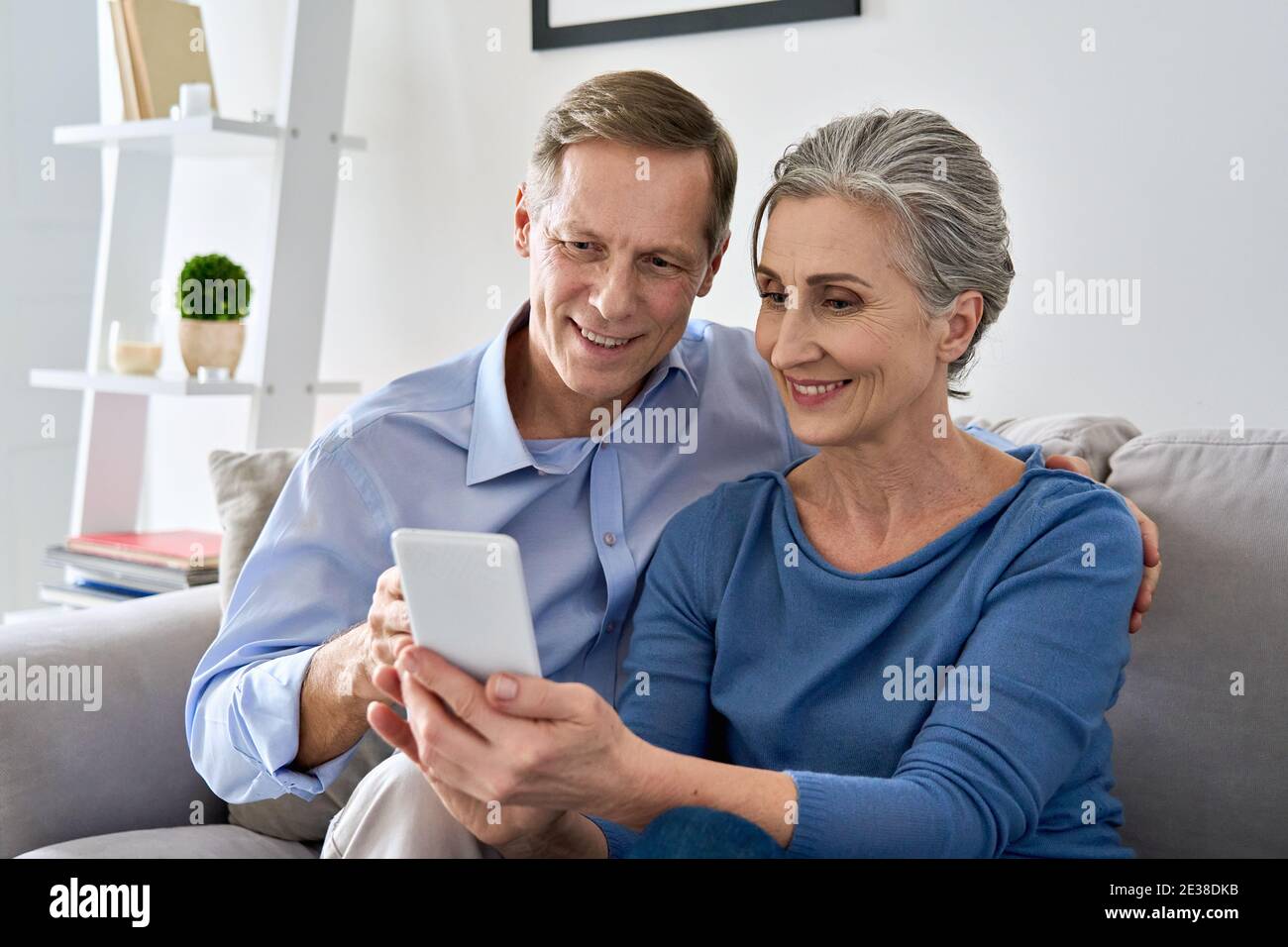 Middle aged couple looking at smartphone using mobile apps sit on sofa at home. Stock Photo
